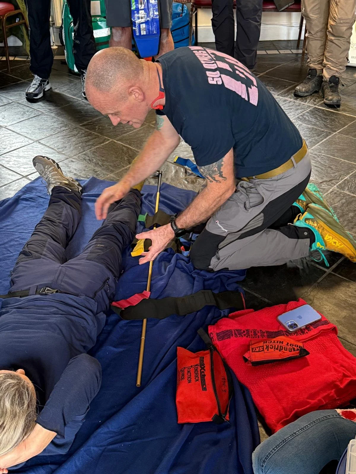 A rescue worker performing first aid on a person lying on the ground, with several onlookers nearby.