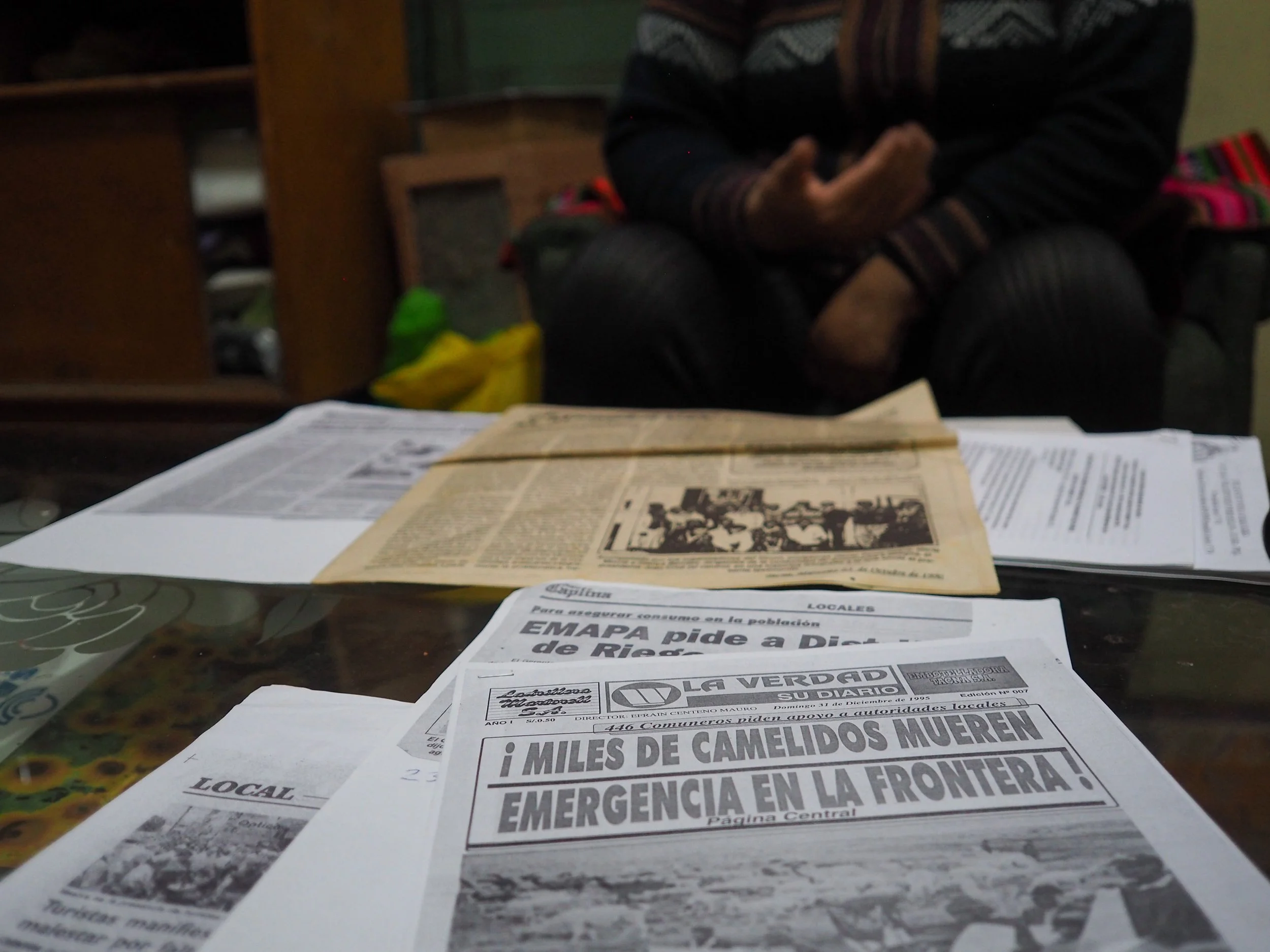 Varias noticias impresas en periódicos sobre una mesa con una persona sentada al fondo.