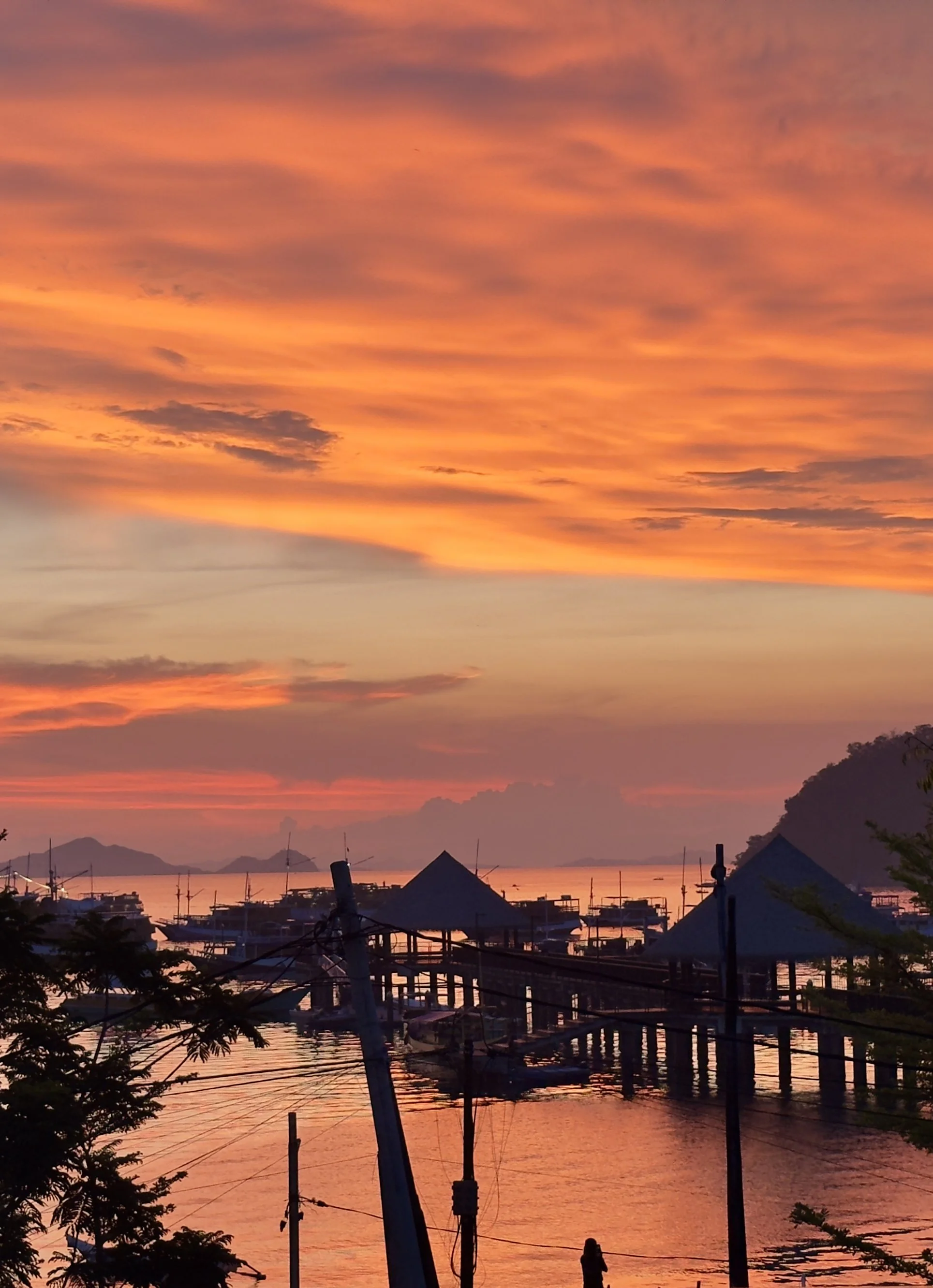 Fiery orange sunset over a harbor with silhouetted boats and a wooden pier