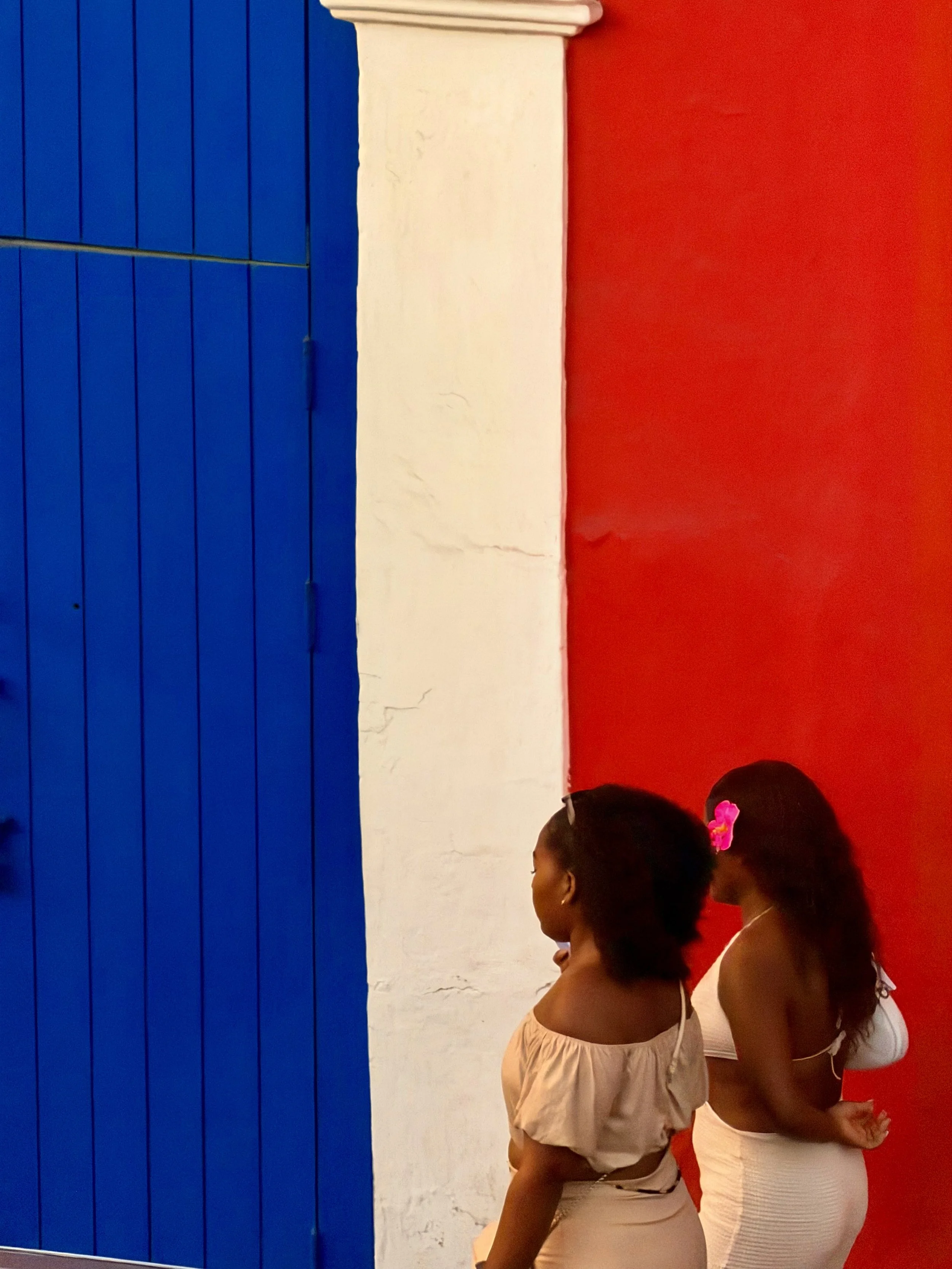 Two girls with flowers in their hair walking past a bold blue, white, and red wall