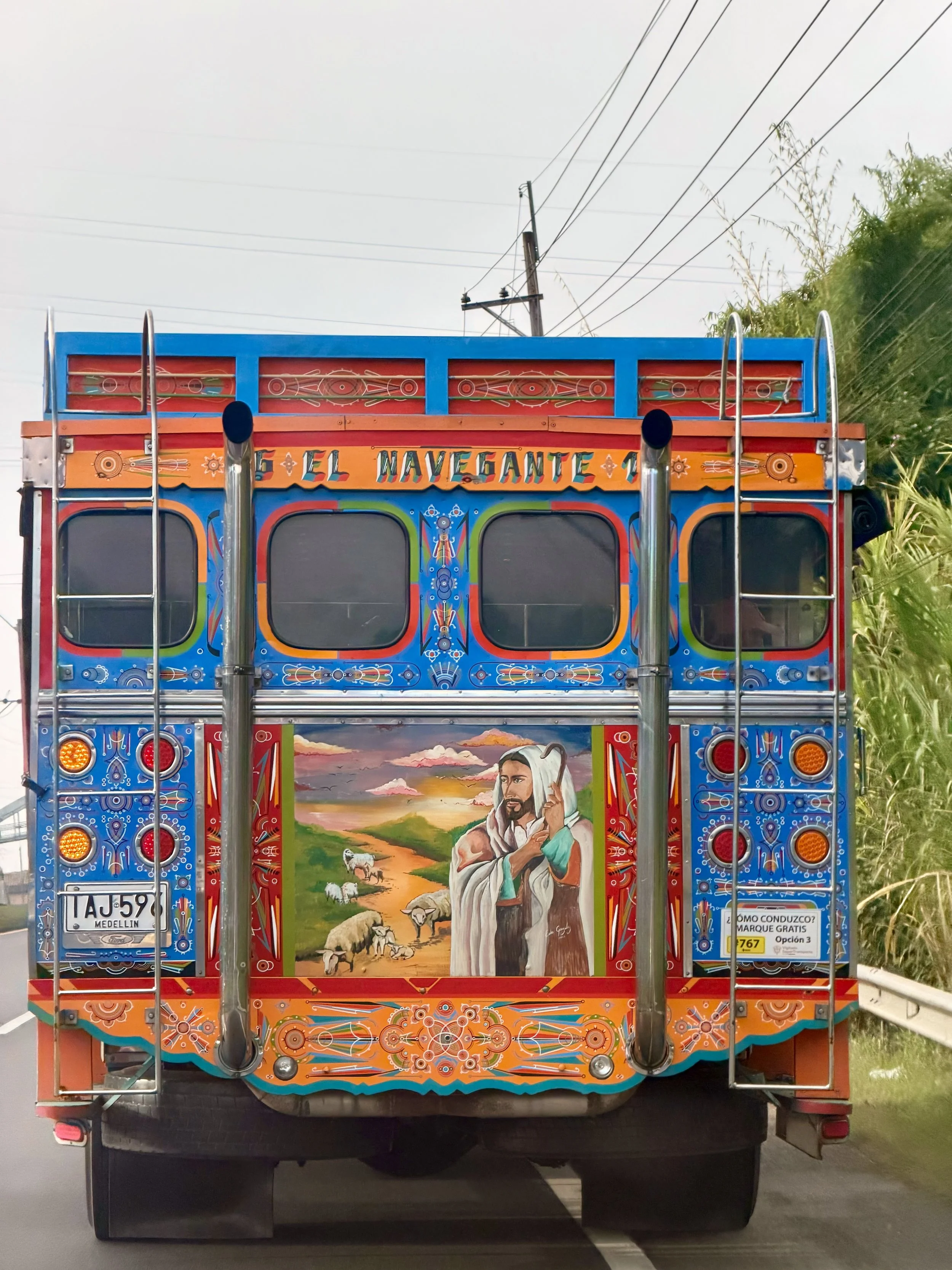 Vividly painted Colombian chiva bus with a hand-painted pastoral mural on its rear