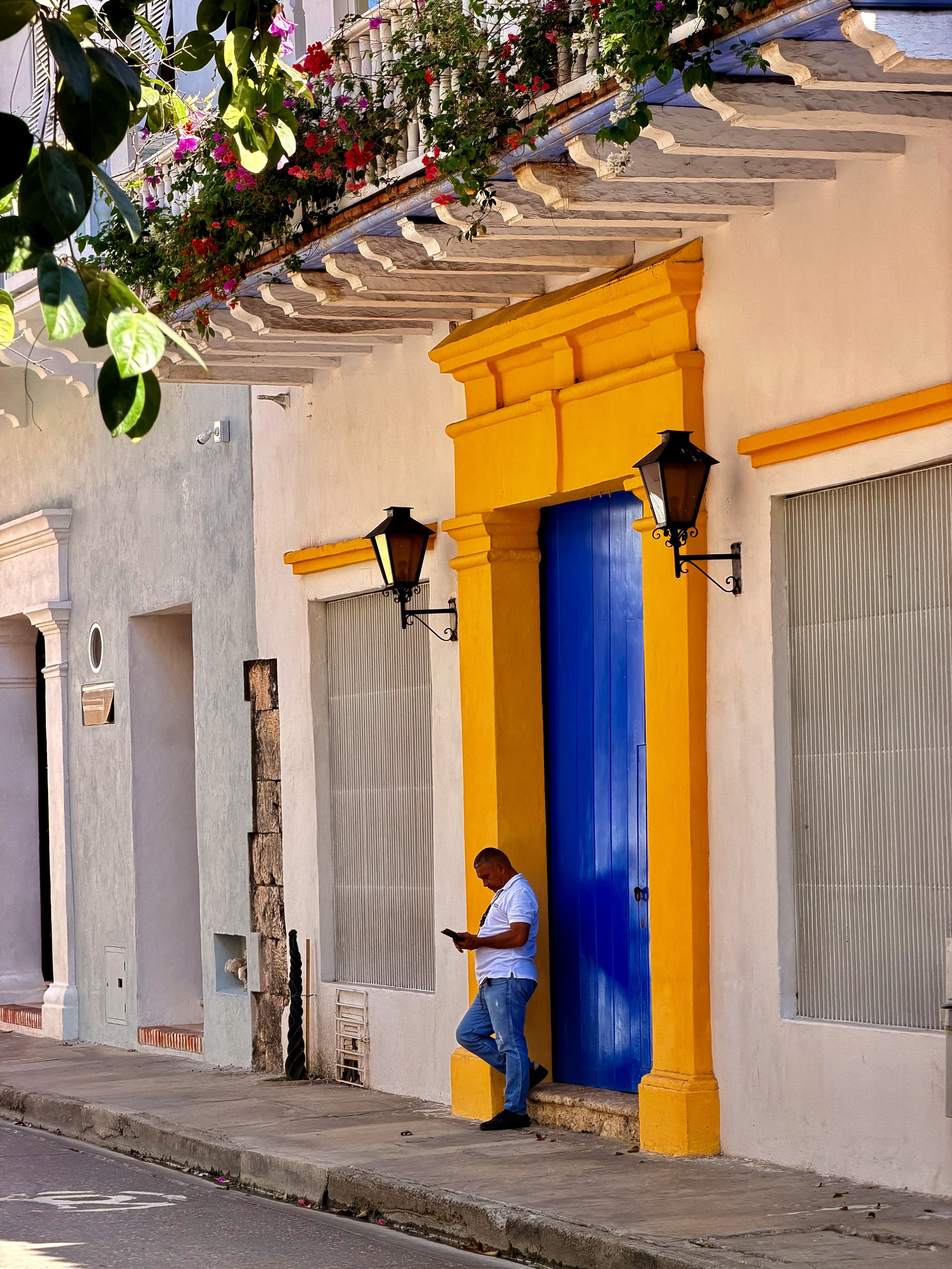 Man checking his phone beside a bright blue doorway with yellow trim on a colonial street