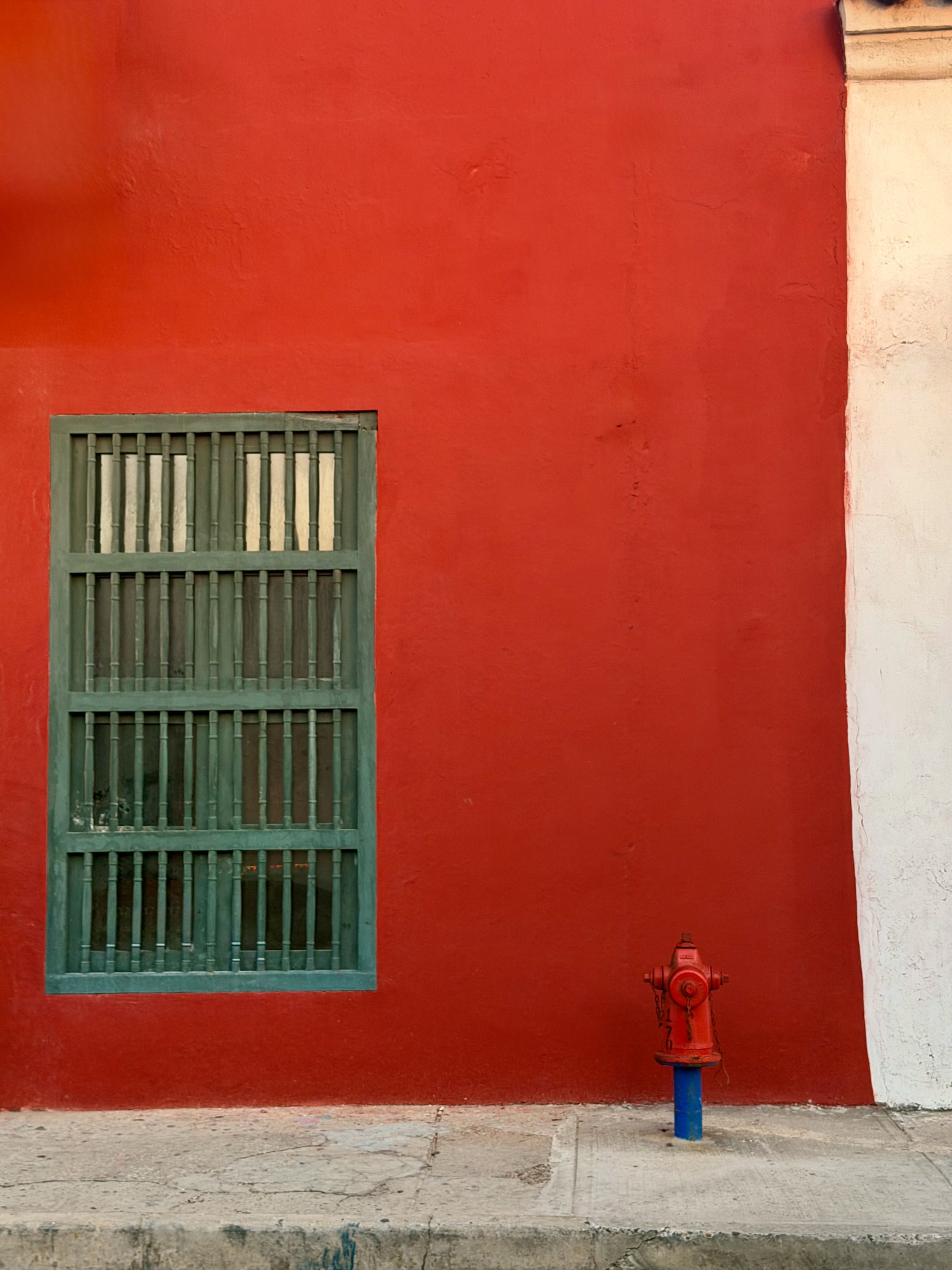 Minimalist red wall with a green barred window and a fire hydrant below