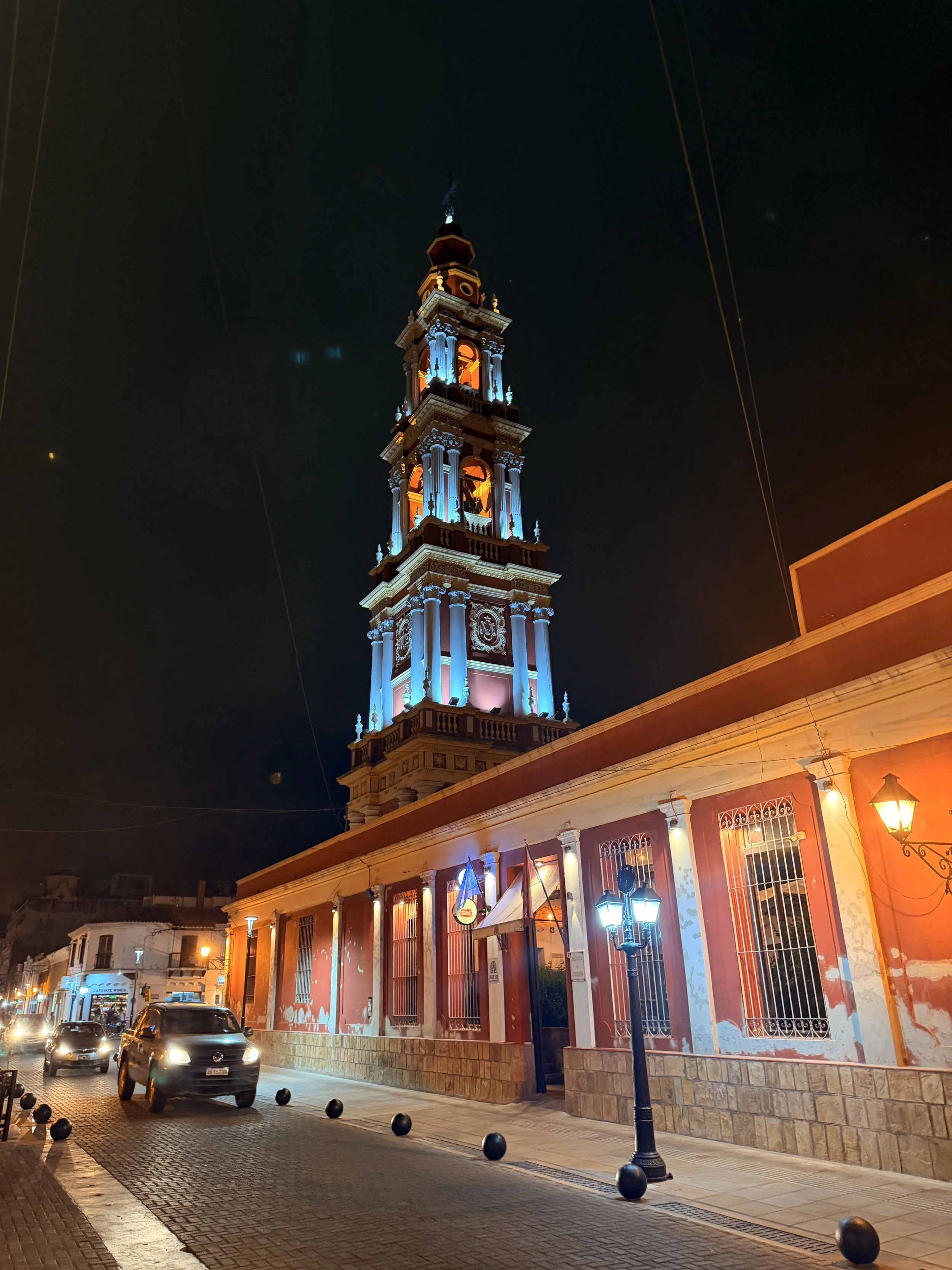 Illuminated bell tower rising above a cobblestone street at night