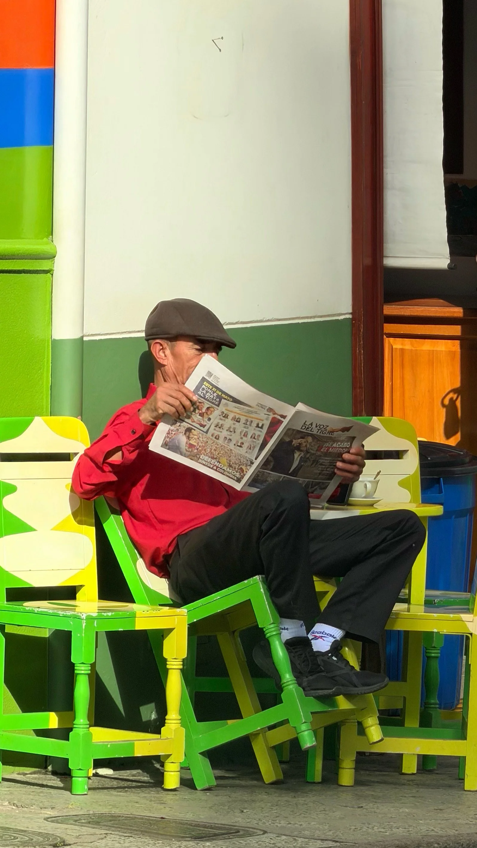 Man reading a newspaper while seated on a bright green chair