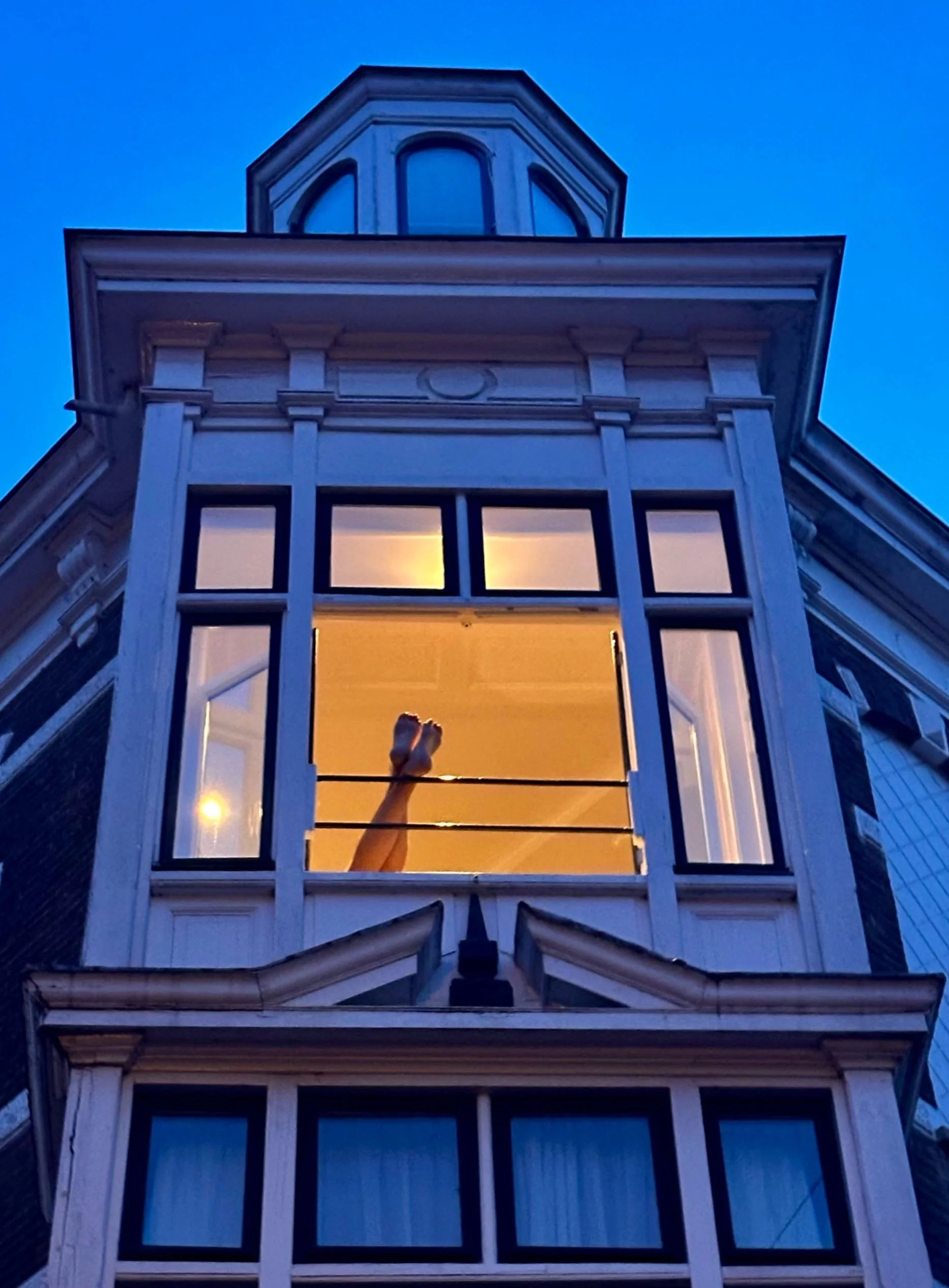 Traditional Amsterdam canal house facade at dusk with a warmly lit window and blue-toned brickwork