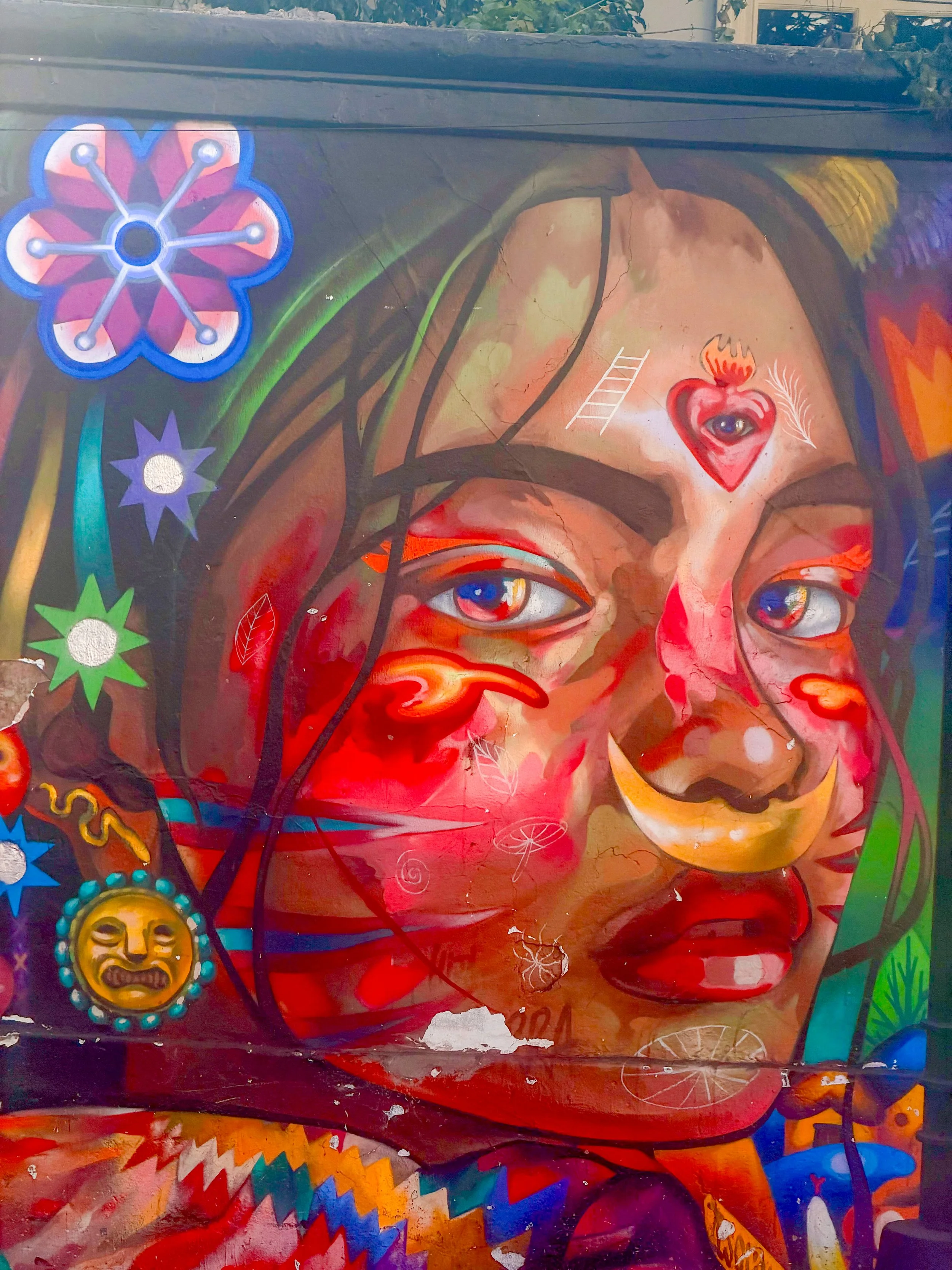 Vibrant street mural of a woman's face adorned with symbolic icons and a nose ring