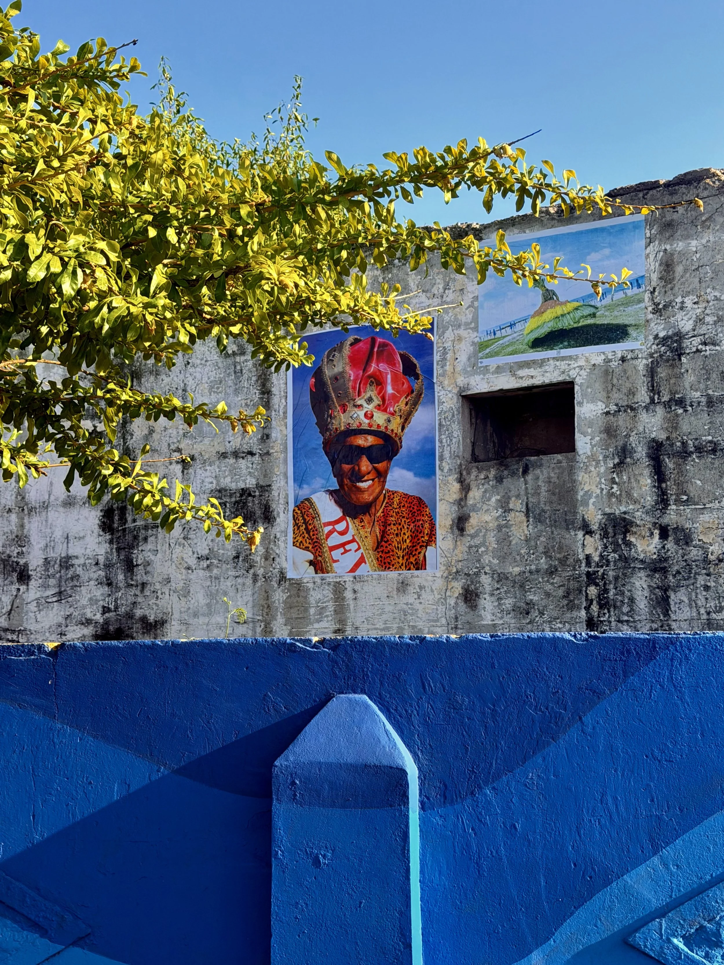 Festival poster on a stone wall above vivid blue paintwork, framed by tree branches