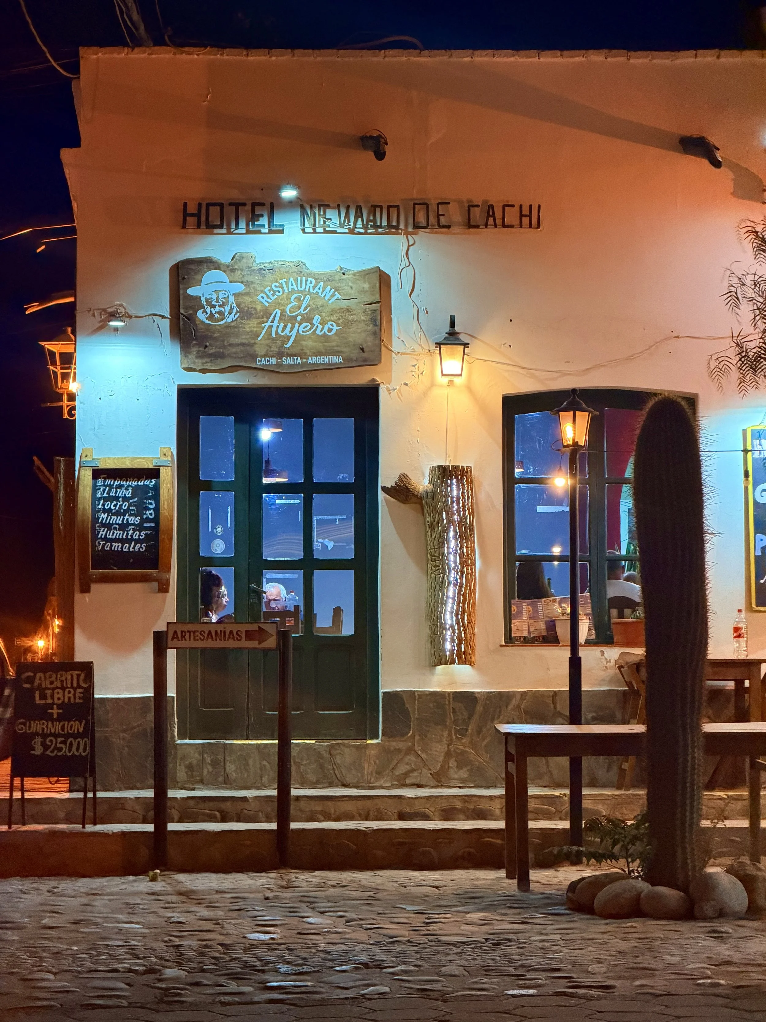 Adobe hotel facade lit up at night with a bench and cactus outside