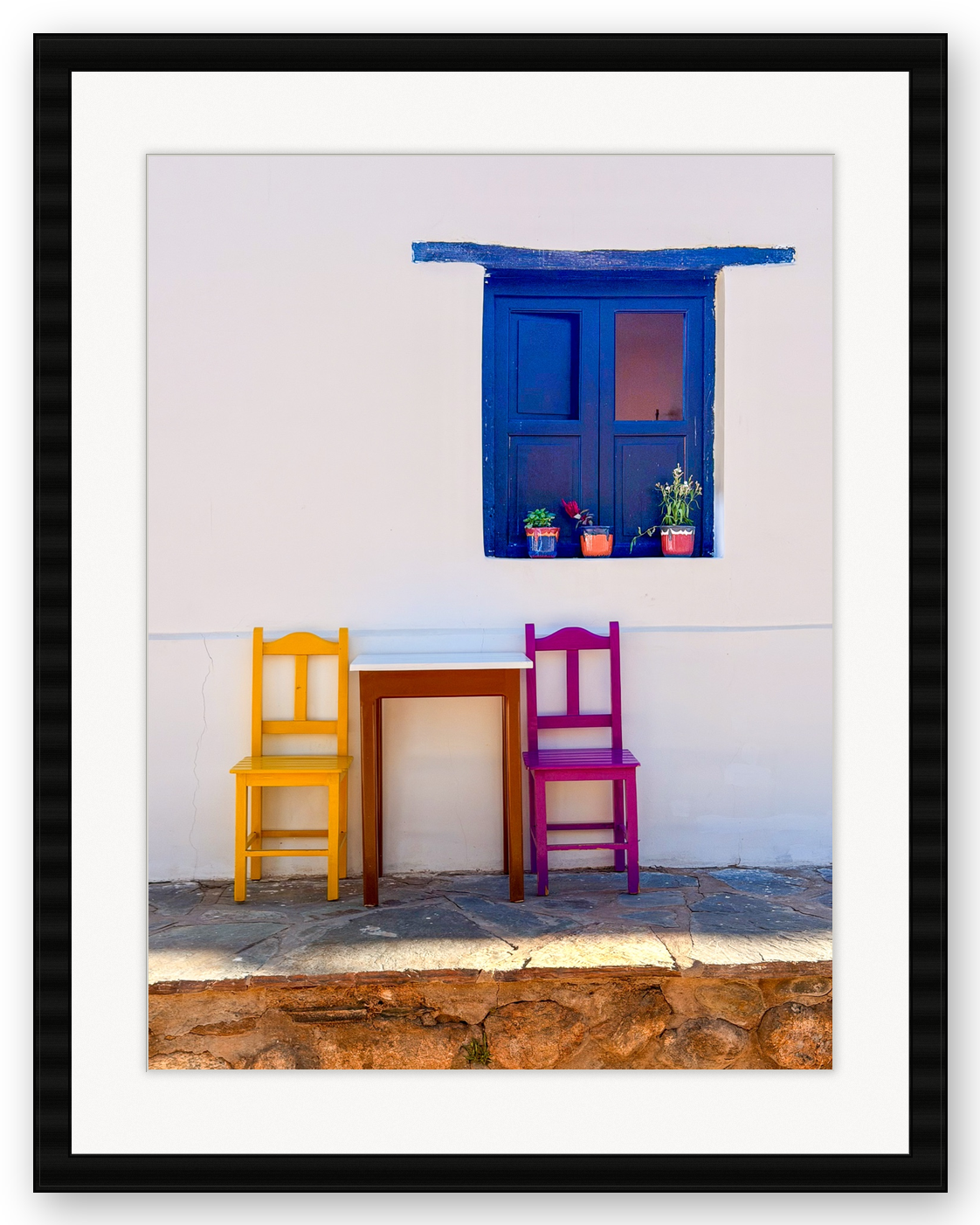 A white wall with a blue window and colorful chairs and flowers underneath.