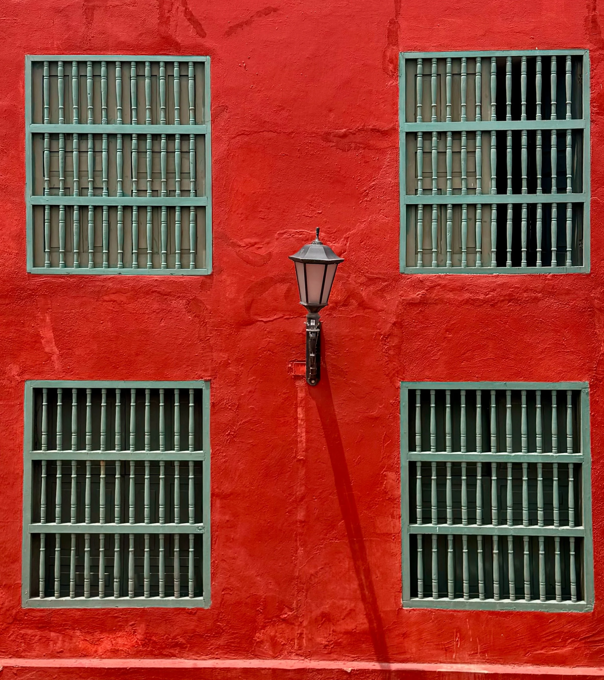 Vivid red building facade with barred windows and a wall-mounted lamp