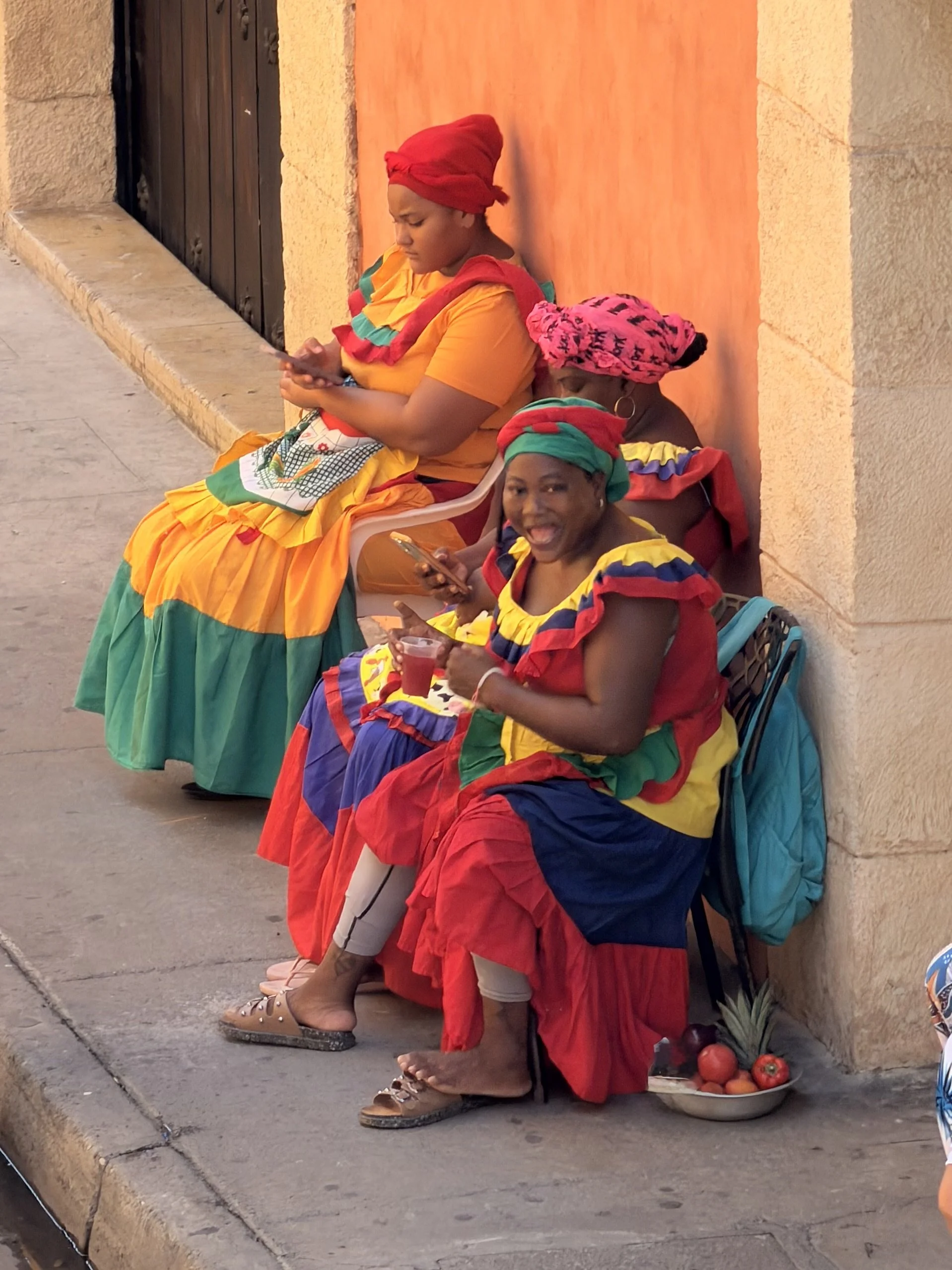 Palenquera fruit vendors in colorful traditional dress resting in a Cartagena doorway