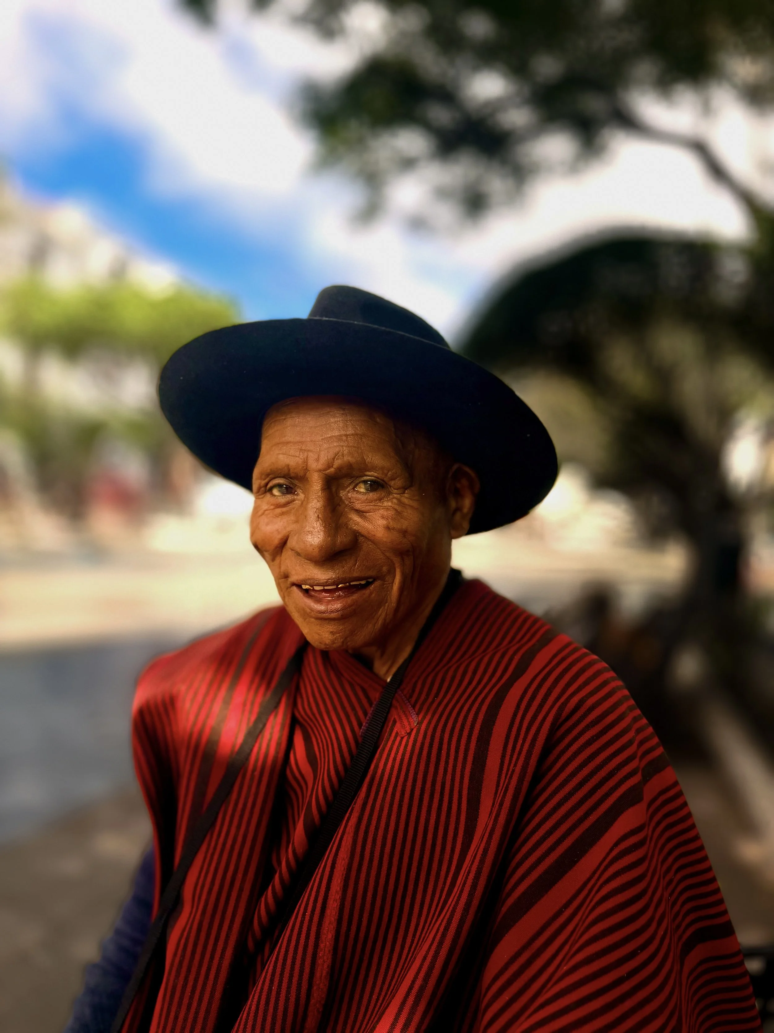 Portrait of a smiling man in a black wide-brimmed hat and red woven poncho