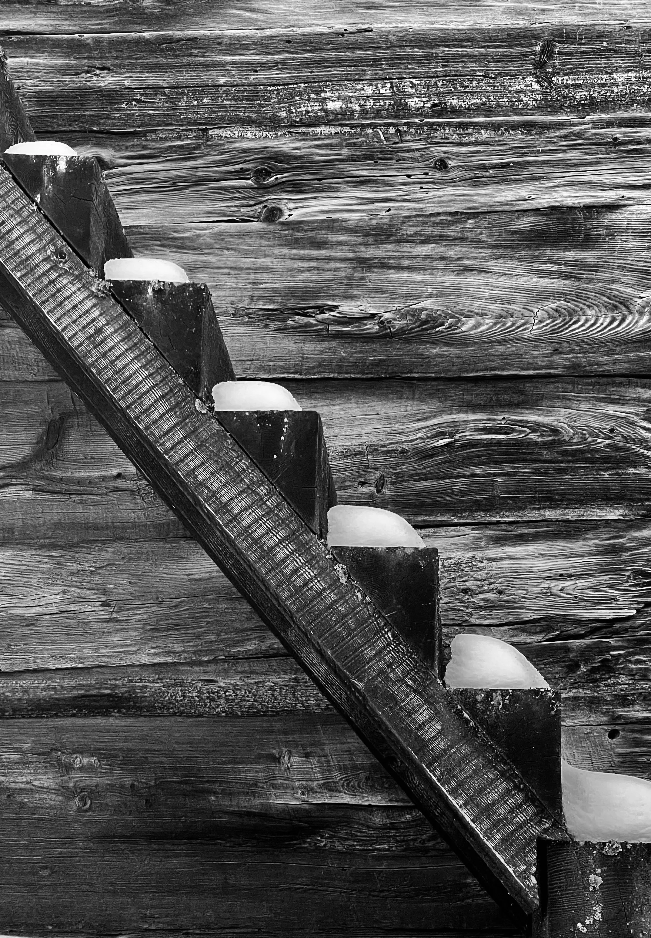 Escher like Black and white photo of a weathered wooden wall with a diagonal wooden stair railing with snow on it. travel-photoraphy