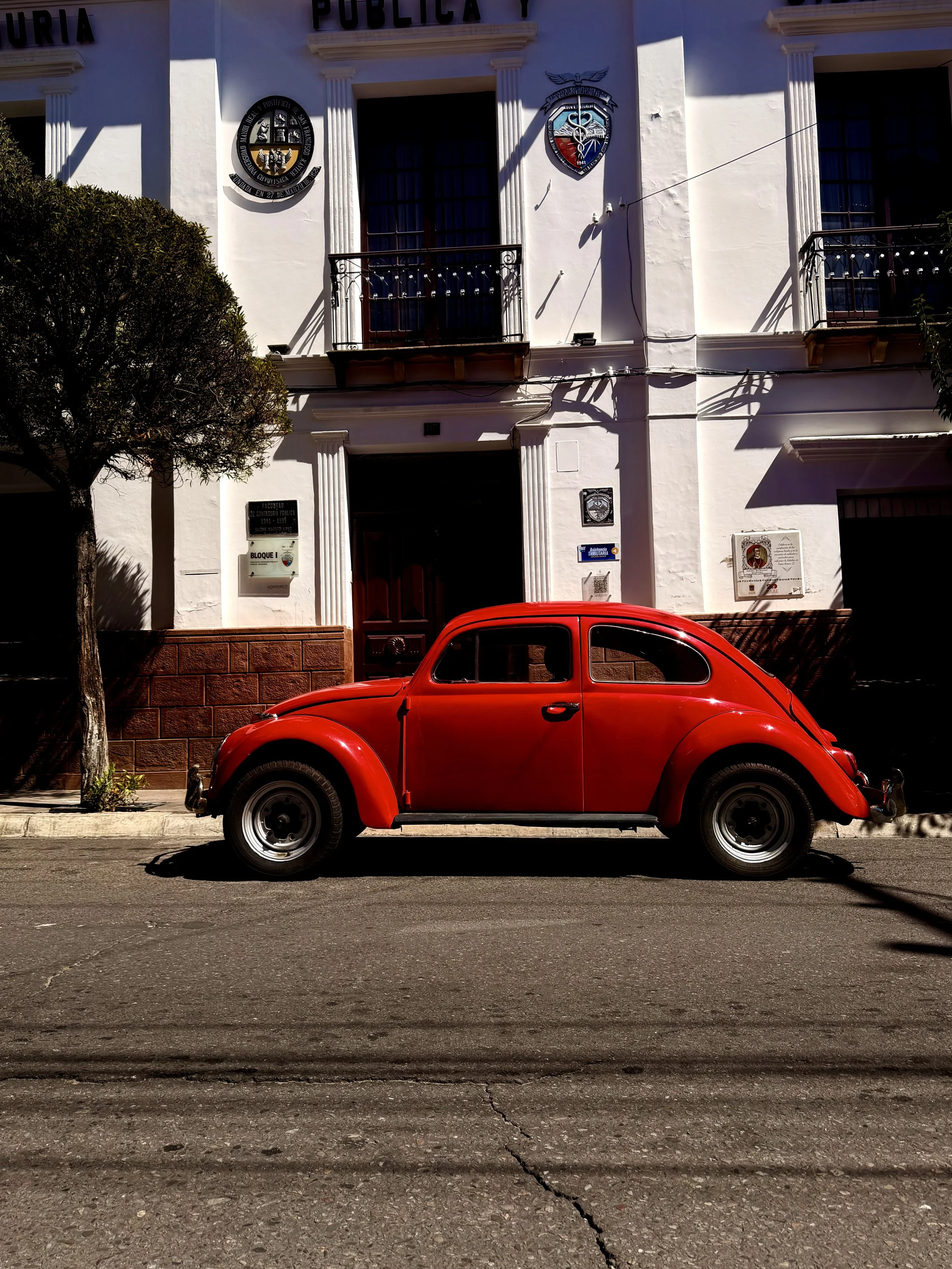 Classic red Volkswagen Beetle parked outside a white colonial building