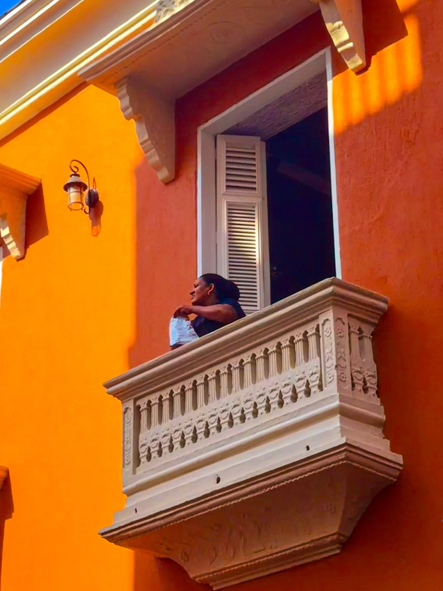 Woman leaning on an ornate white balcony against a bold orange facade