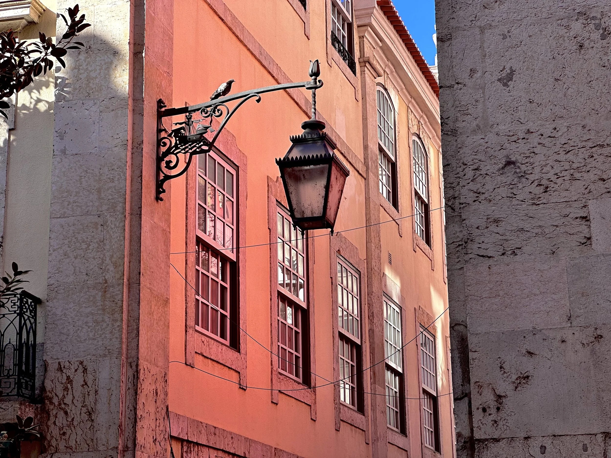 Ornate hanging street lamp on a coral-pink building facade with tall shuttered windows