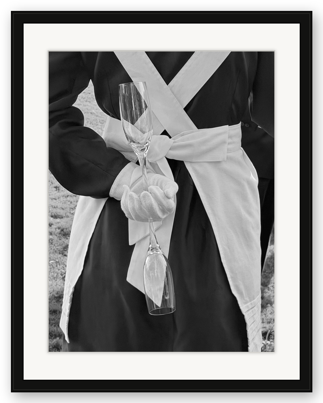 Person in historical uniform holding two empty champagne flutes in black and white photograph.