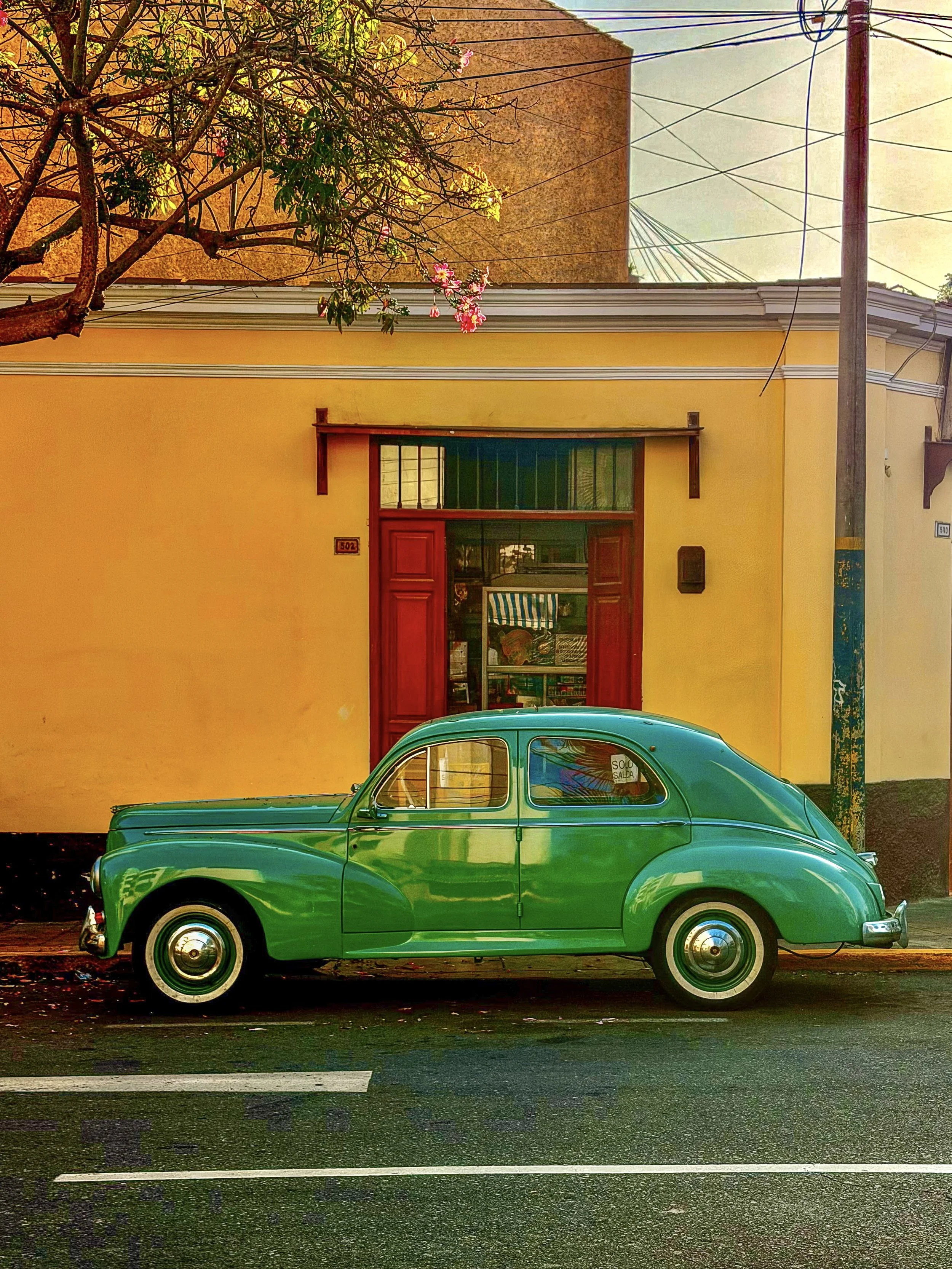 Vintage green car parked outside a yellow building with a red door