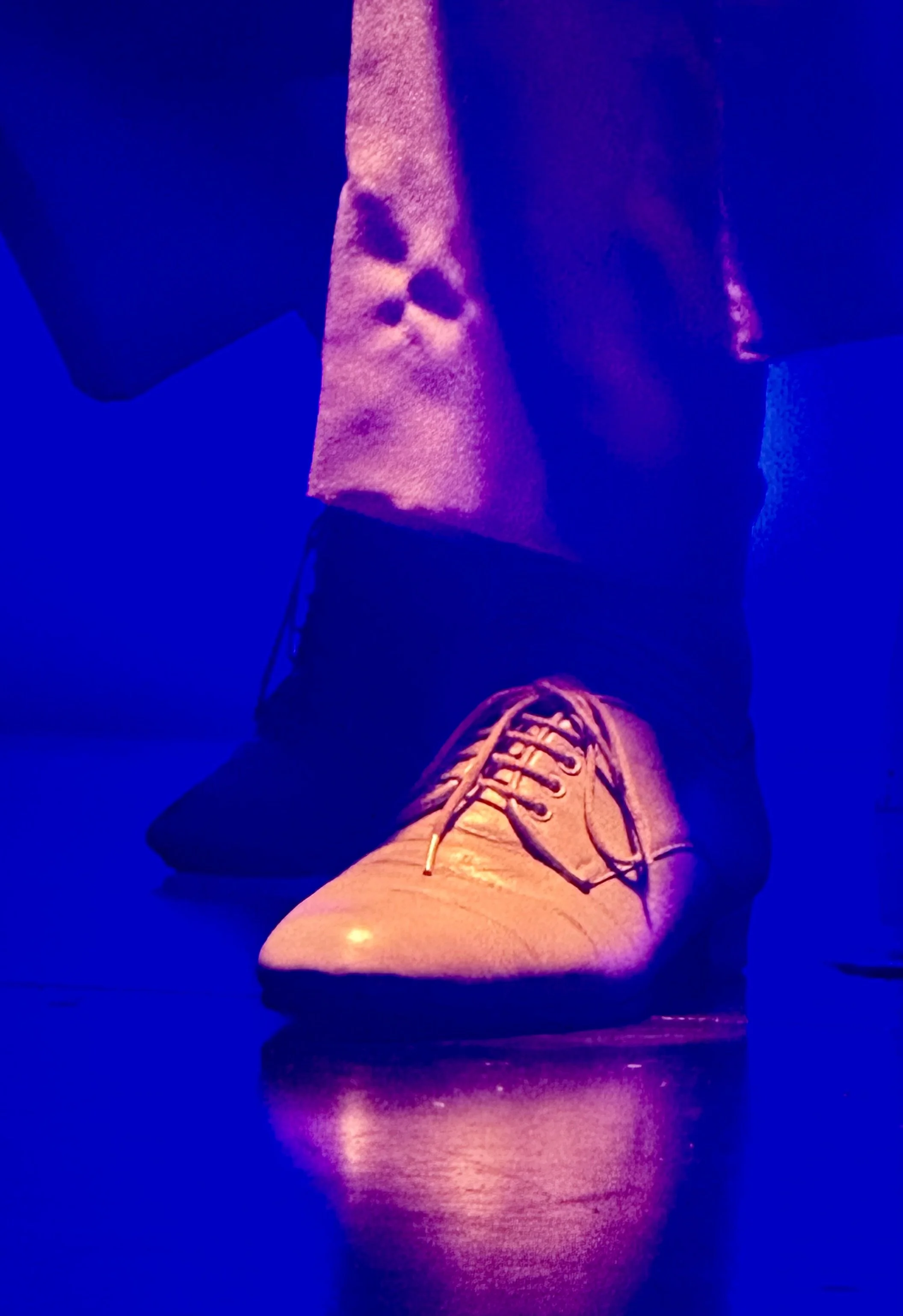 Dancer's shoe glowing under dramatic blue and orange stage lighting