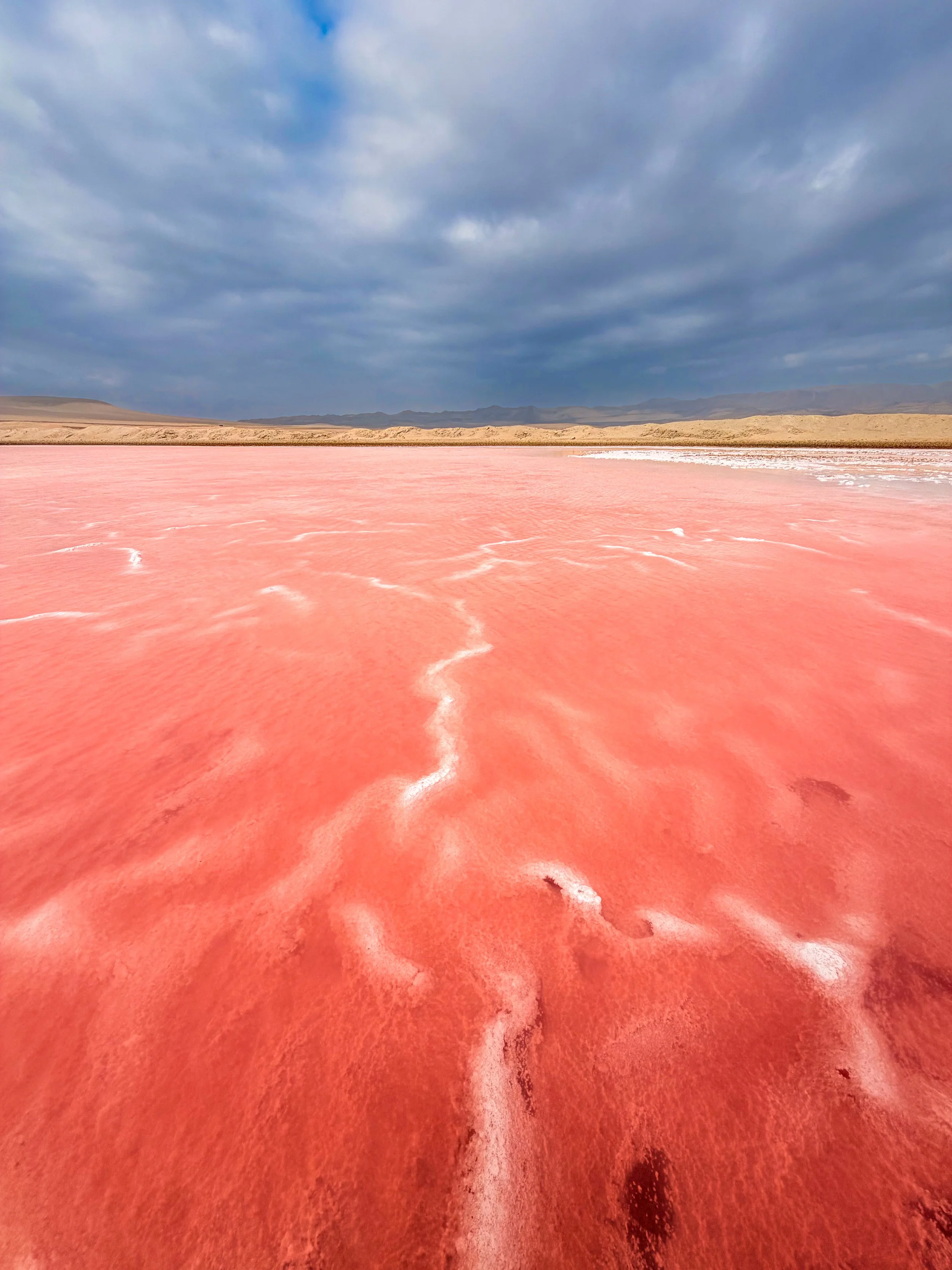 Vivid pink salt lake beneath a dramatic stormy sky