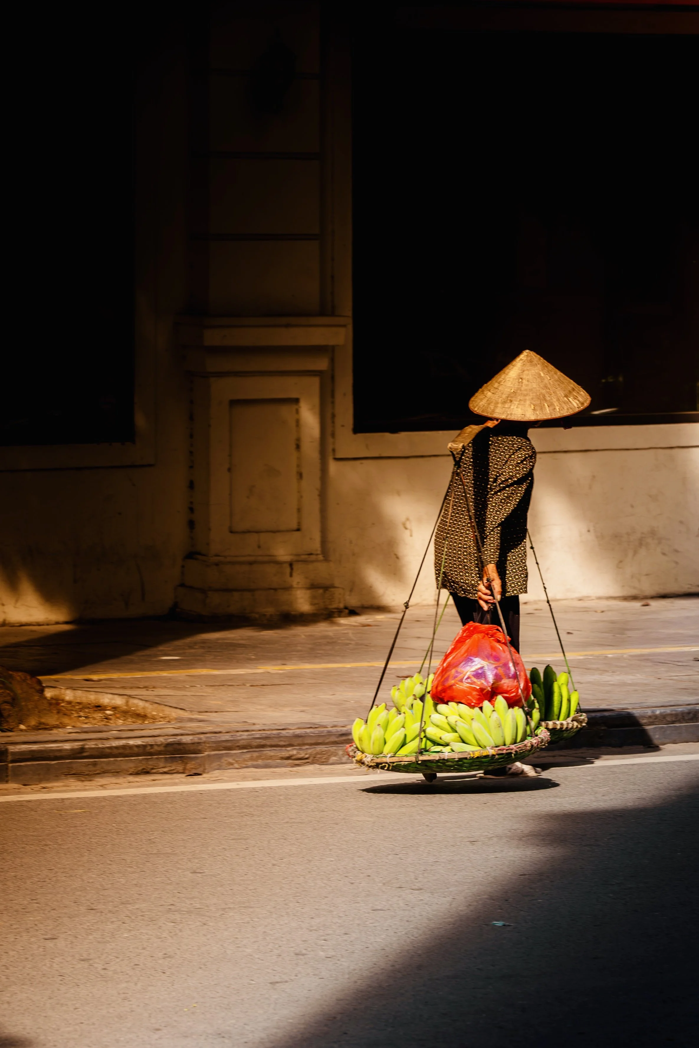 A street vendor with traditional Asian conical hat selling bananas in early morning light