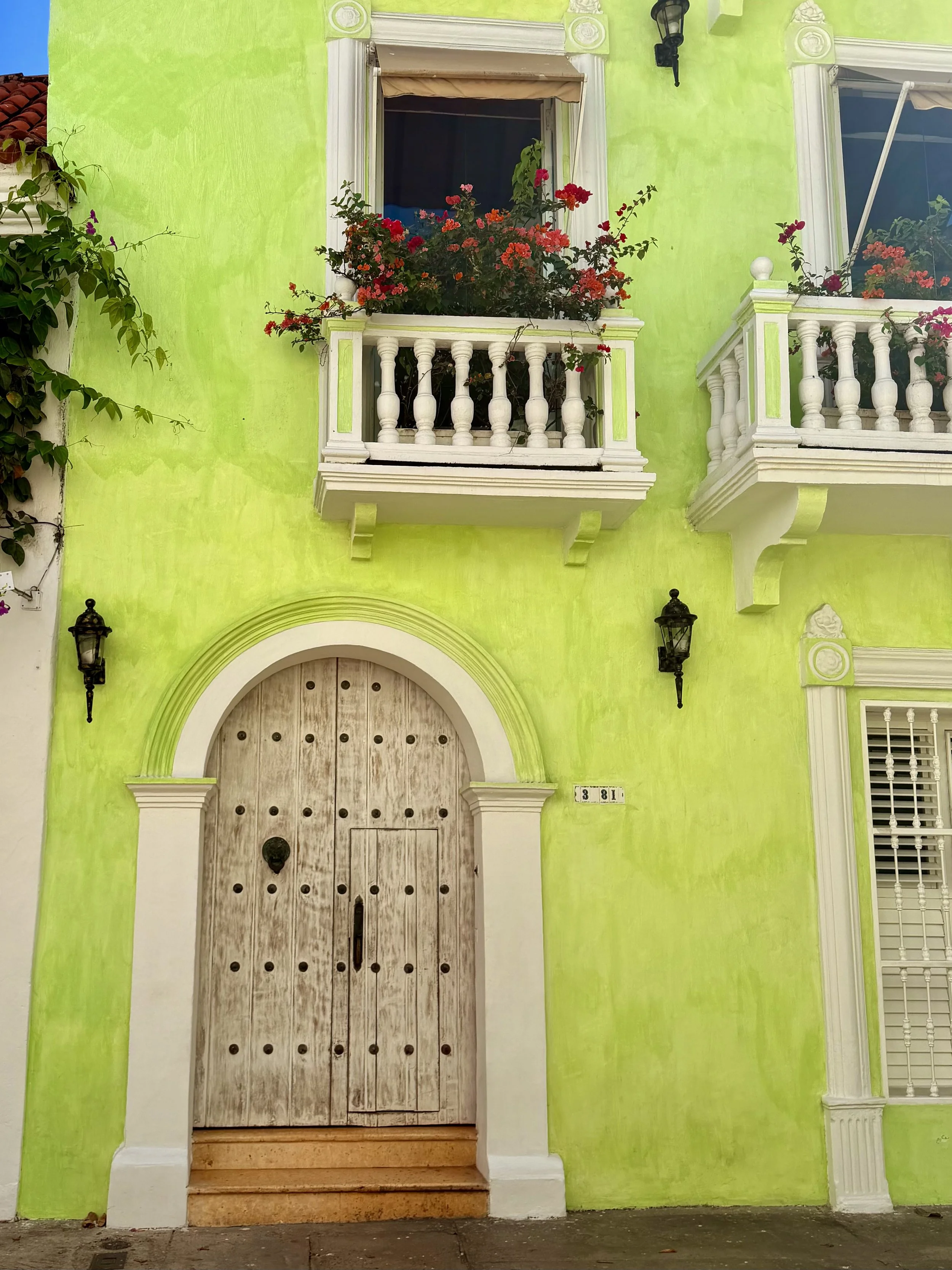 Bright green colonial facade with flower-filled balconies and a carved wooden door