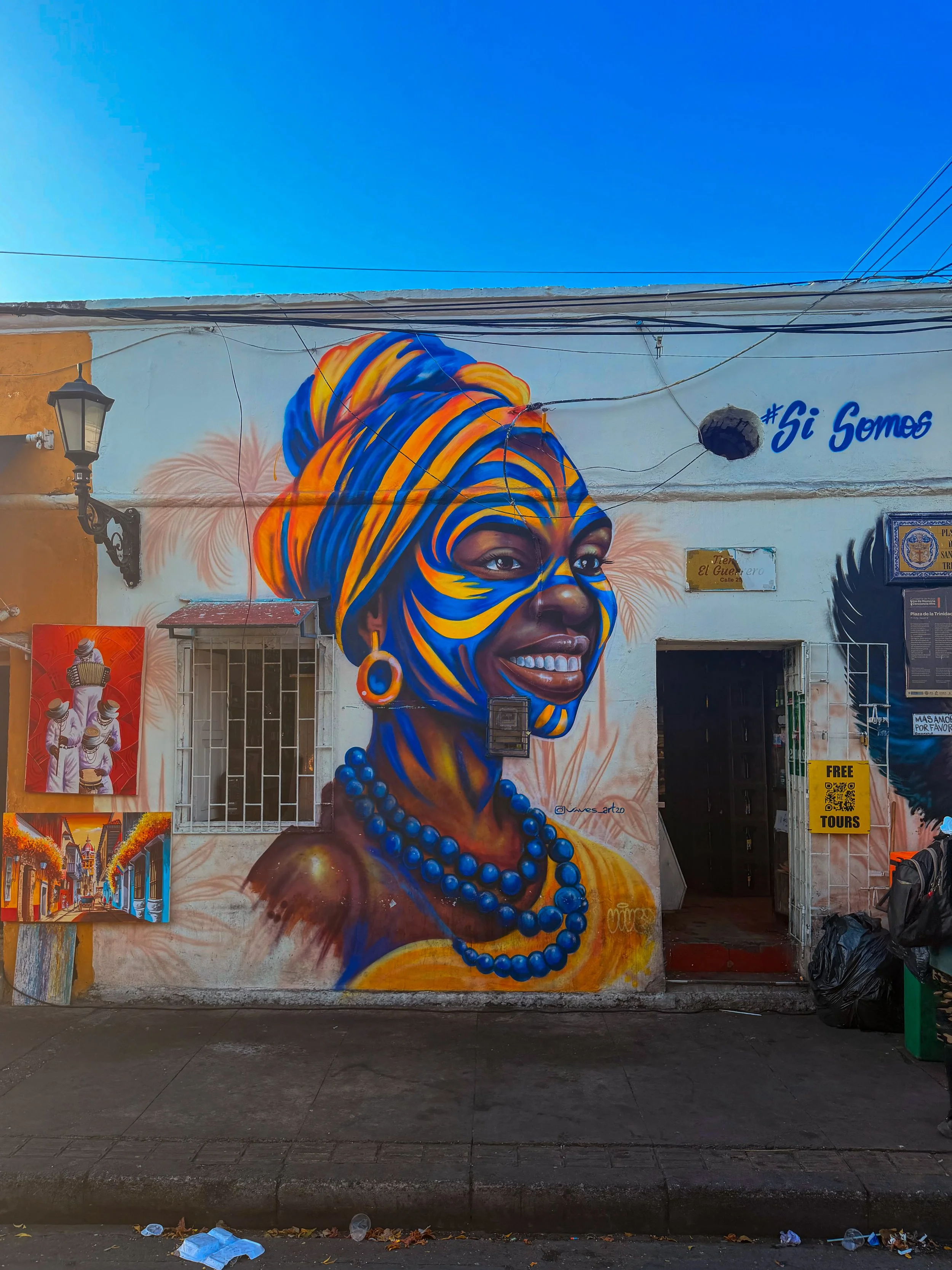 Large street mural of a woman in a blue headwrap and beaded jewelry