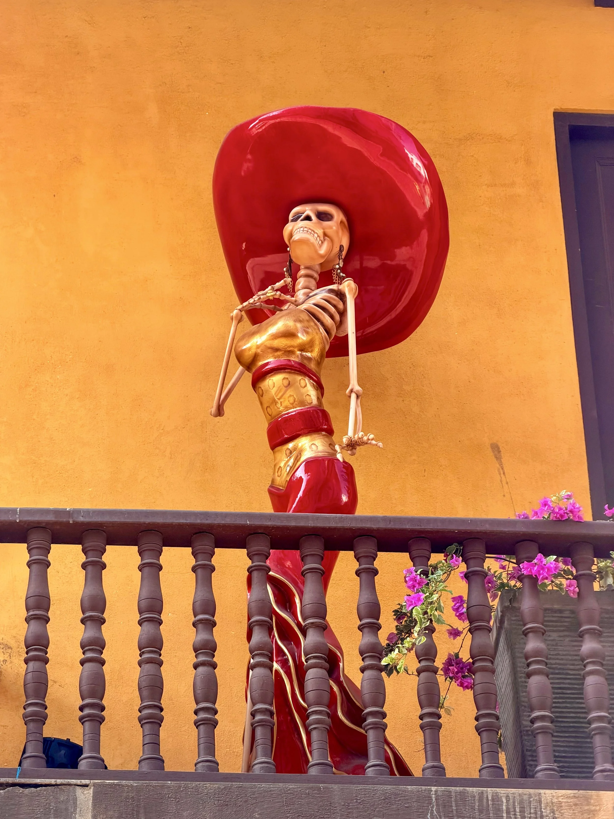 Ornate Catrina skeleton figure in a red hat and gold dress on a balcony