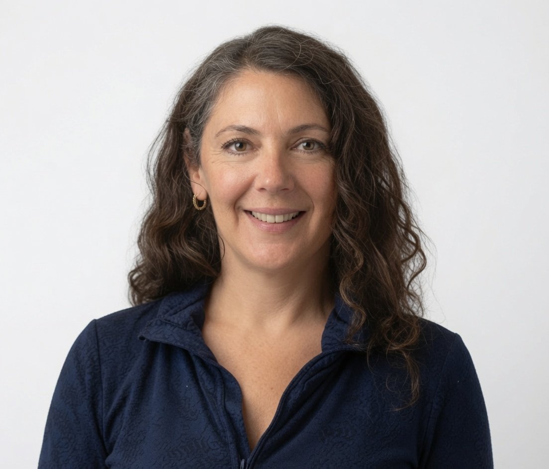 Joyce Roetter pictured with shoulder-length brown curly hair, wearing a navy blue zip-up jacket, smiling, with a plain light-colored background.