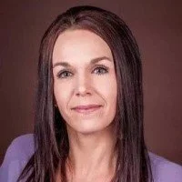 A woman with long brown hair wearing a purple blazer against a plain background.
