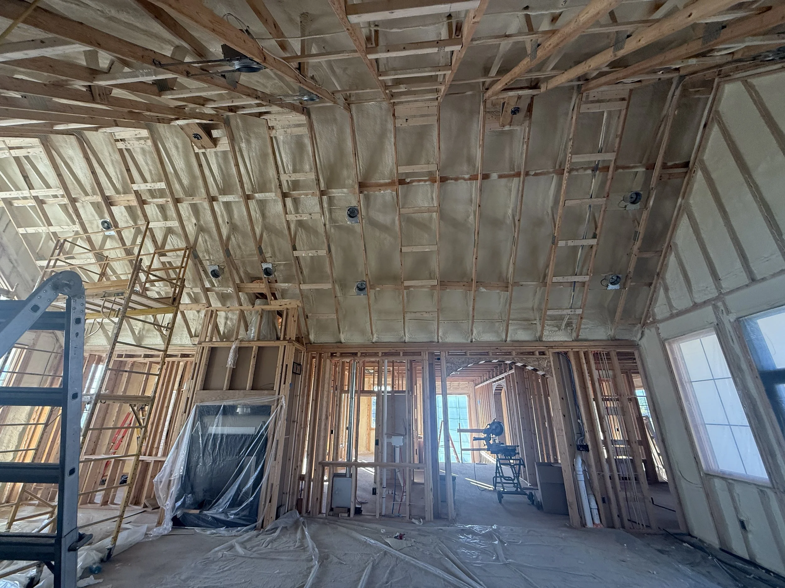 Interior of a house under construction, showing wooden framing, insulation, and construction tools.