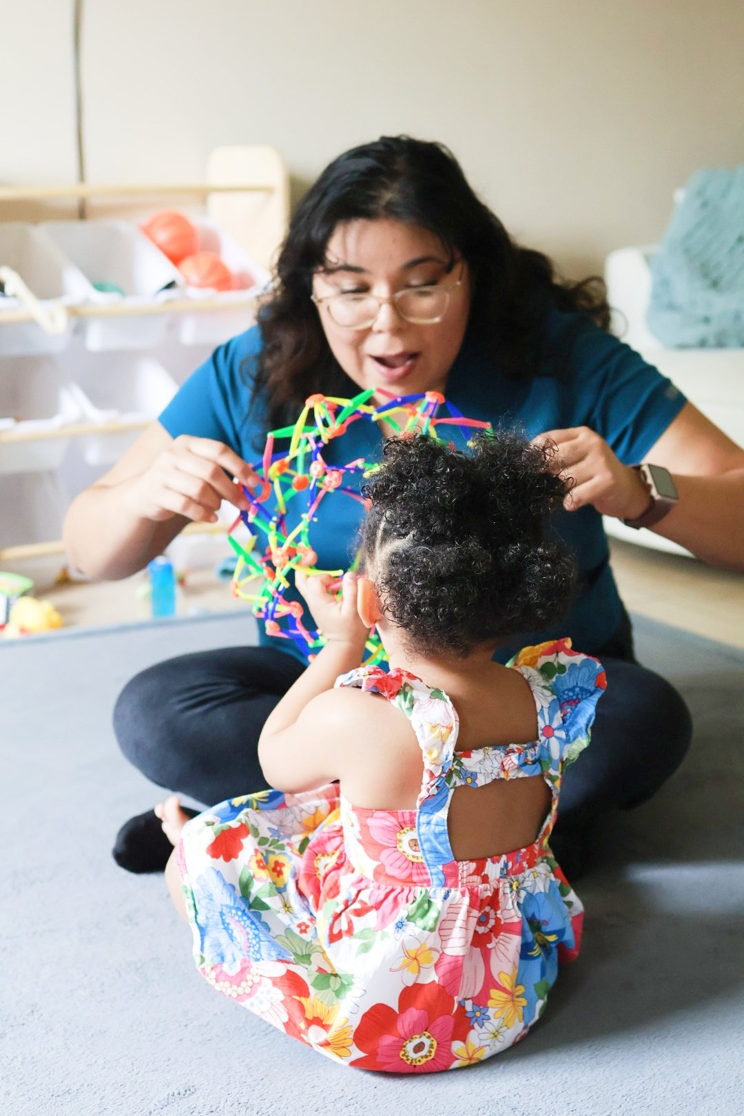 A woman and a young girl playing with colorful bendable toys indoors.