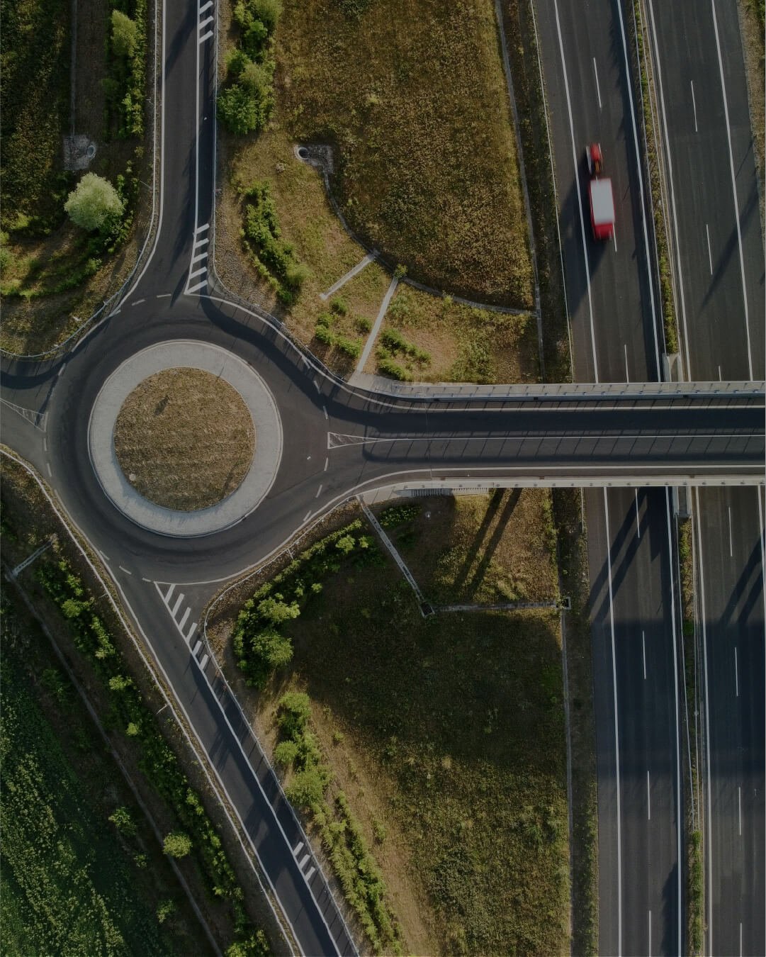 Aerial view of a highway interchange with a roundabout, transitioning from a curved road to a multi-lane highway, with greenery and trees along the roads.