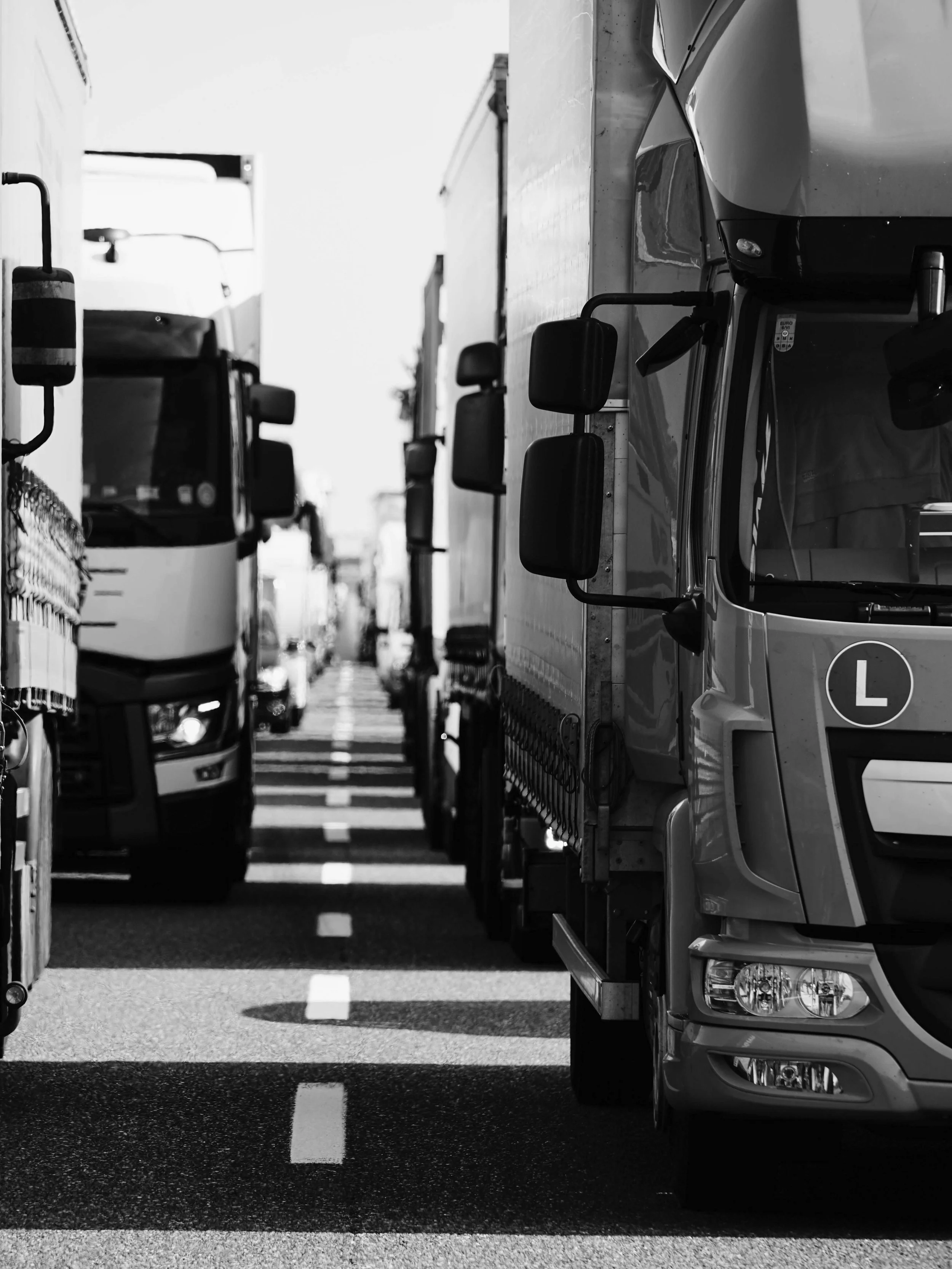Black and white photo of trucks parked closely together on a road with a dashed line running down the center.