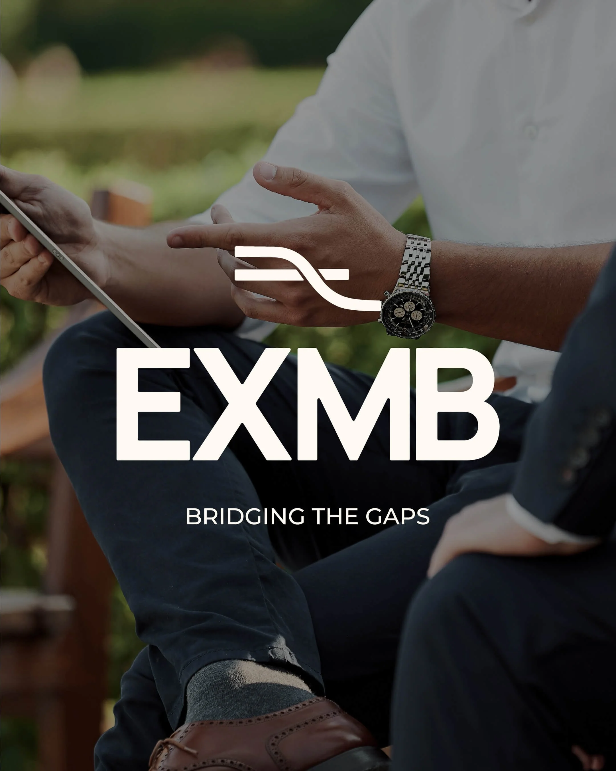 Person in a white shirt holding a tablet in an outdoor setting in a business meeting with the text 'EXMB' and 'Bridging the Gaps' overlaid on the image.