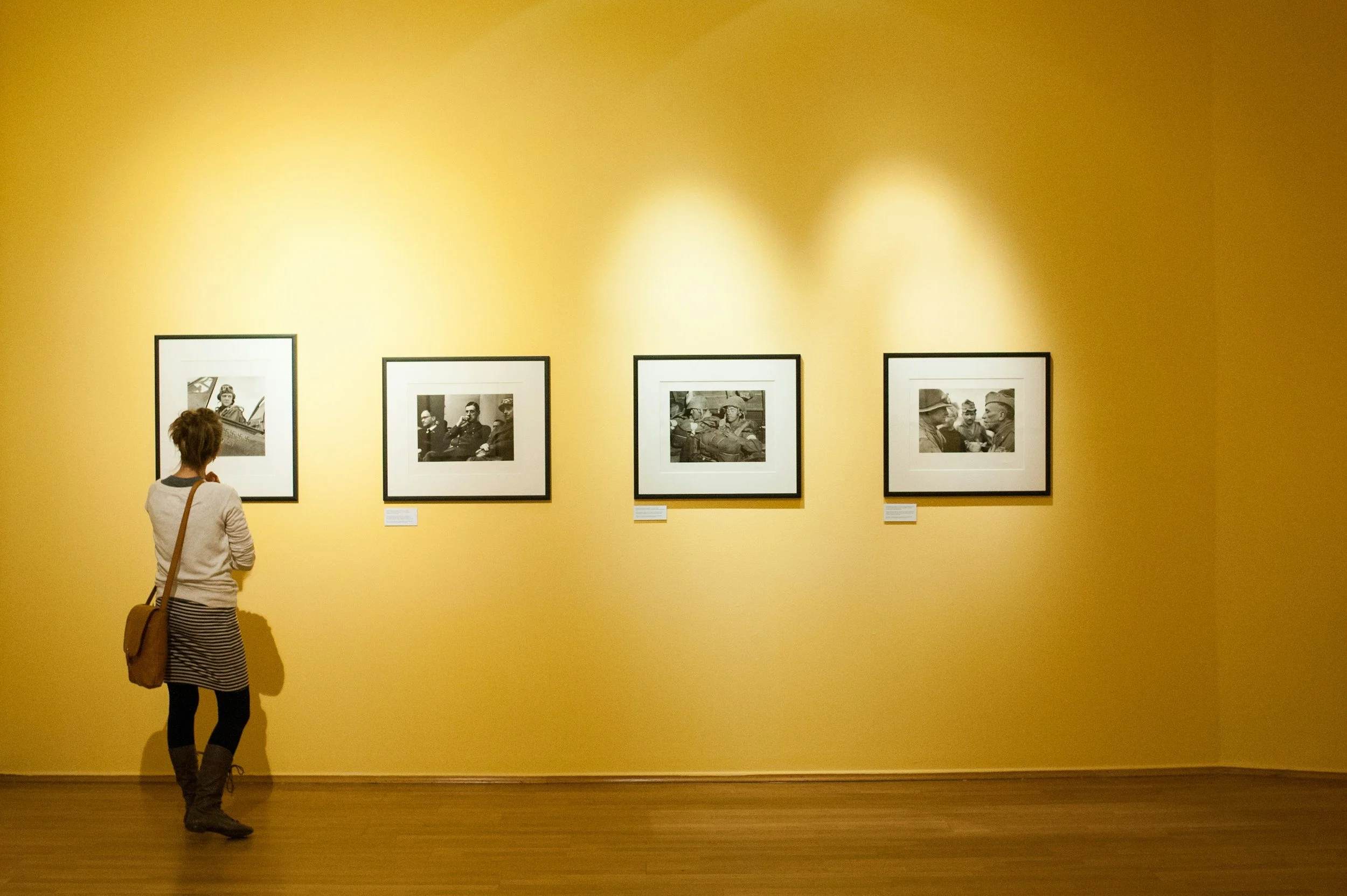 Person observing black and white photographs on yellow gallery wall.