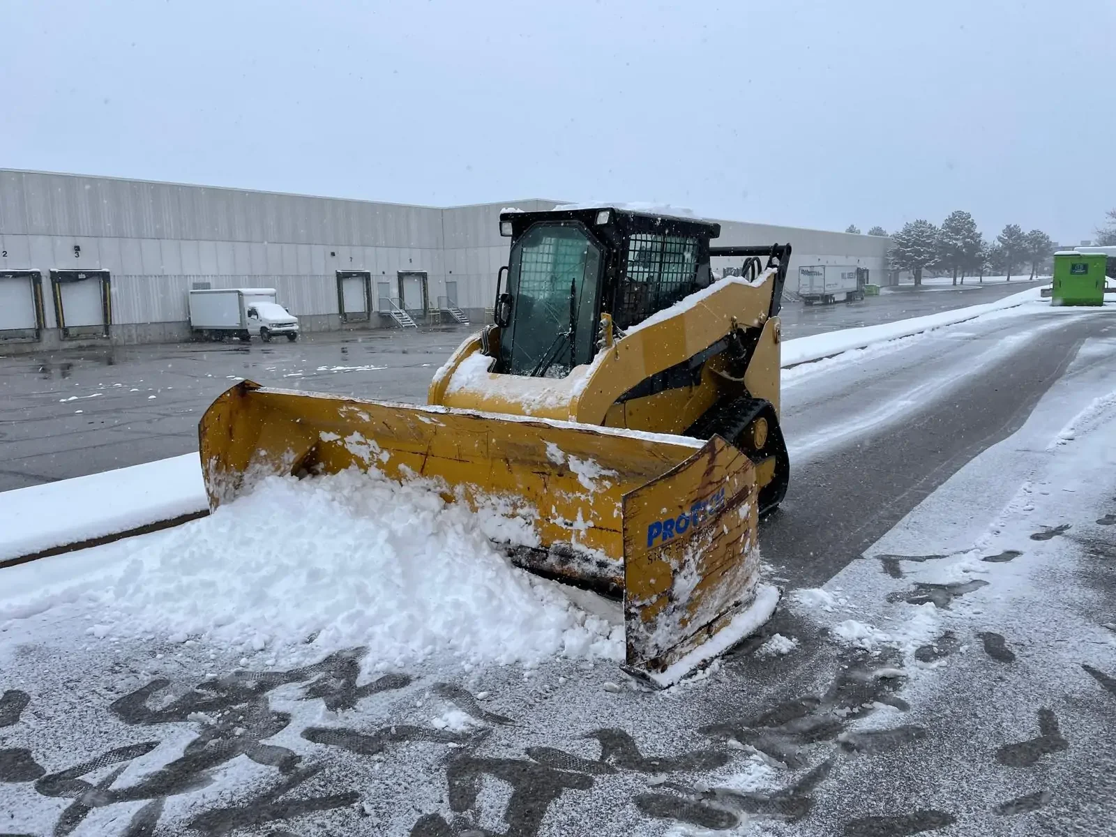 A yellow snowplow clearing snow from a parking lot on a snowy day.