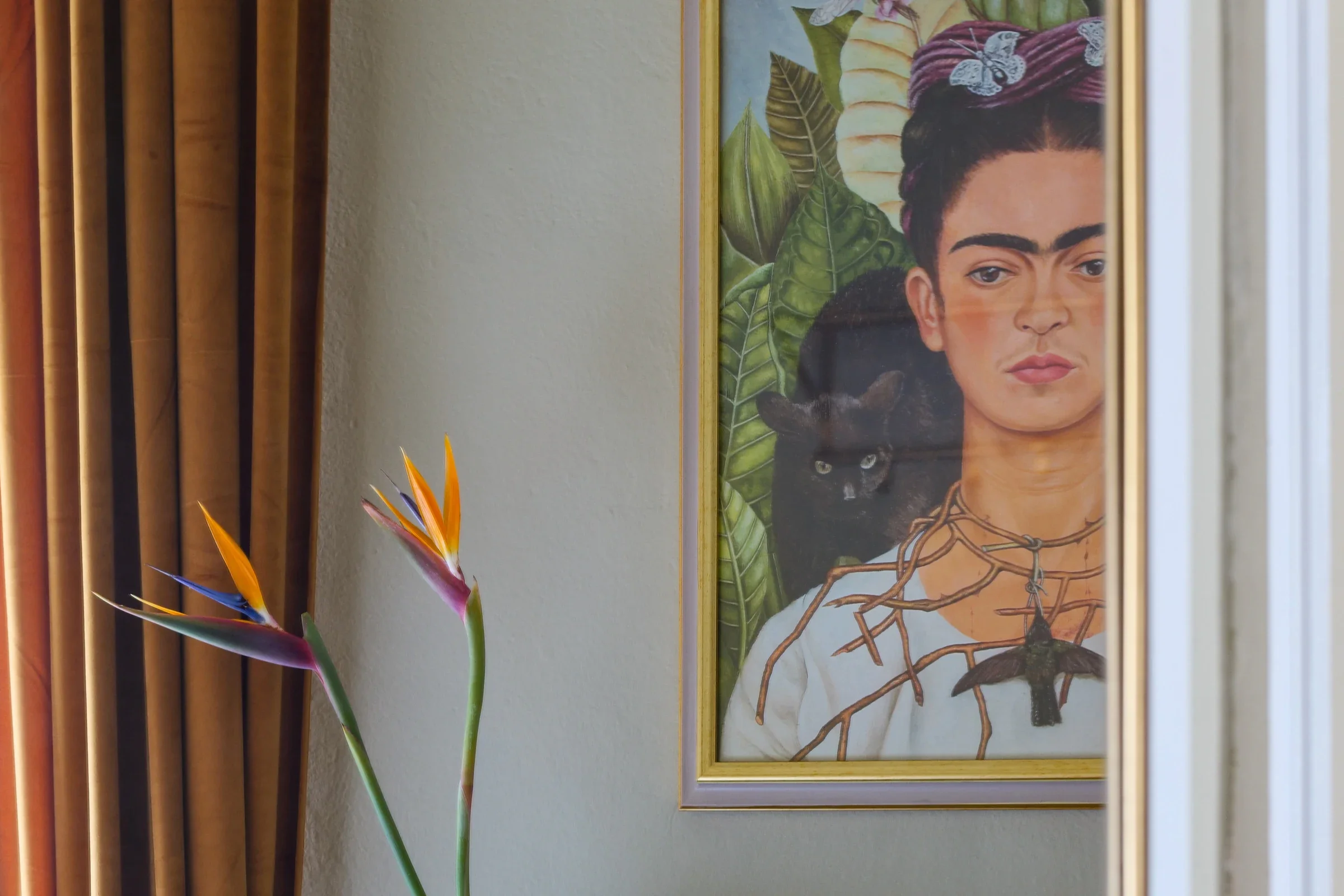 Framed Frida Kahlo painting with bird-of-paradise flowers and a velvet curtain