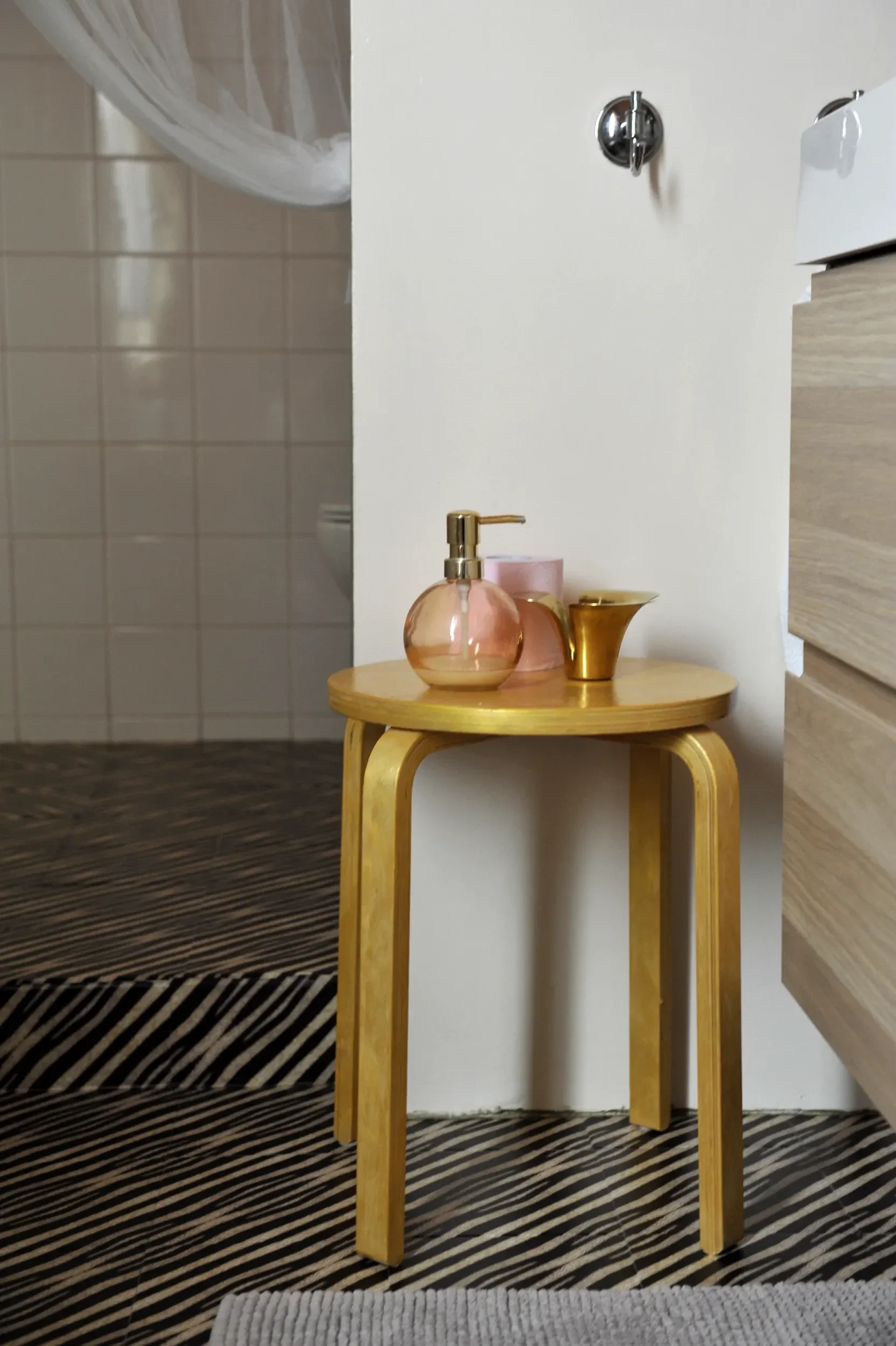 Gold Aalto stool with a pink glass soap dispenser on the  animelier tile-skin floor