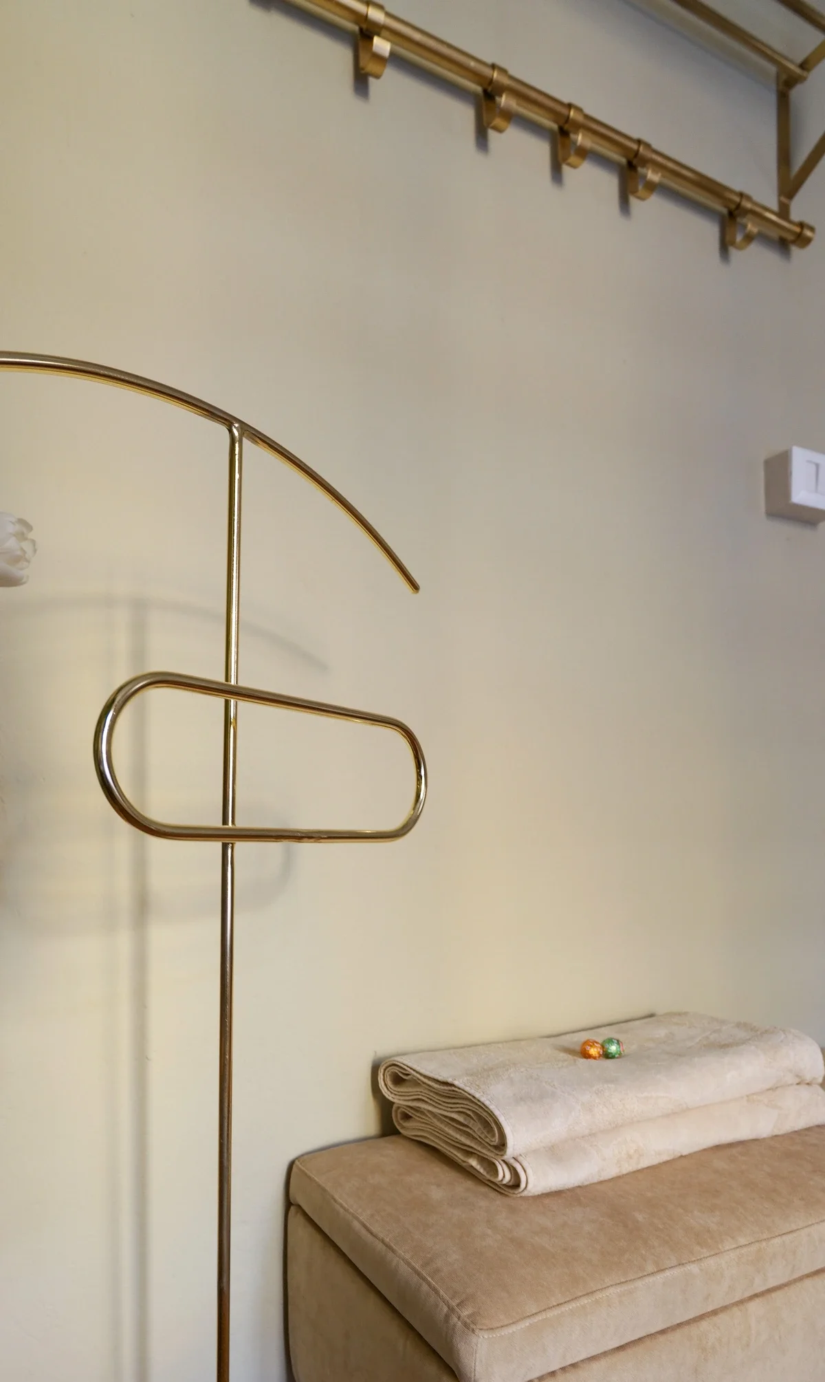 Brass valet stand beside the velvet bench with folded towels and the gold coat rail