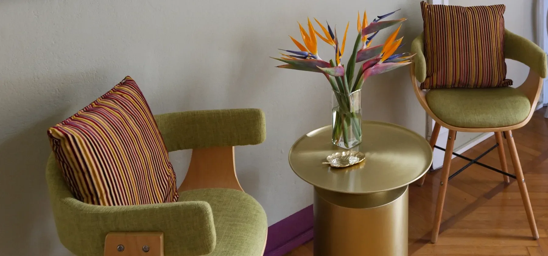 Green Rubelli armchairs around the 101 Copenhagen brushed brass table with bird-of-paradise flowers
