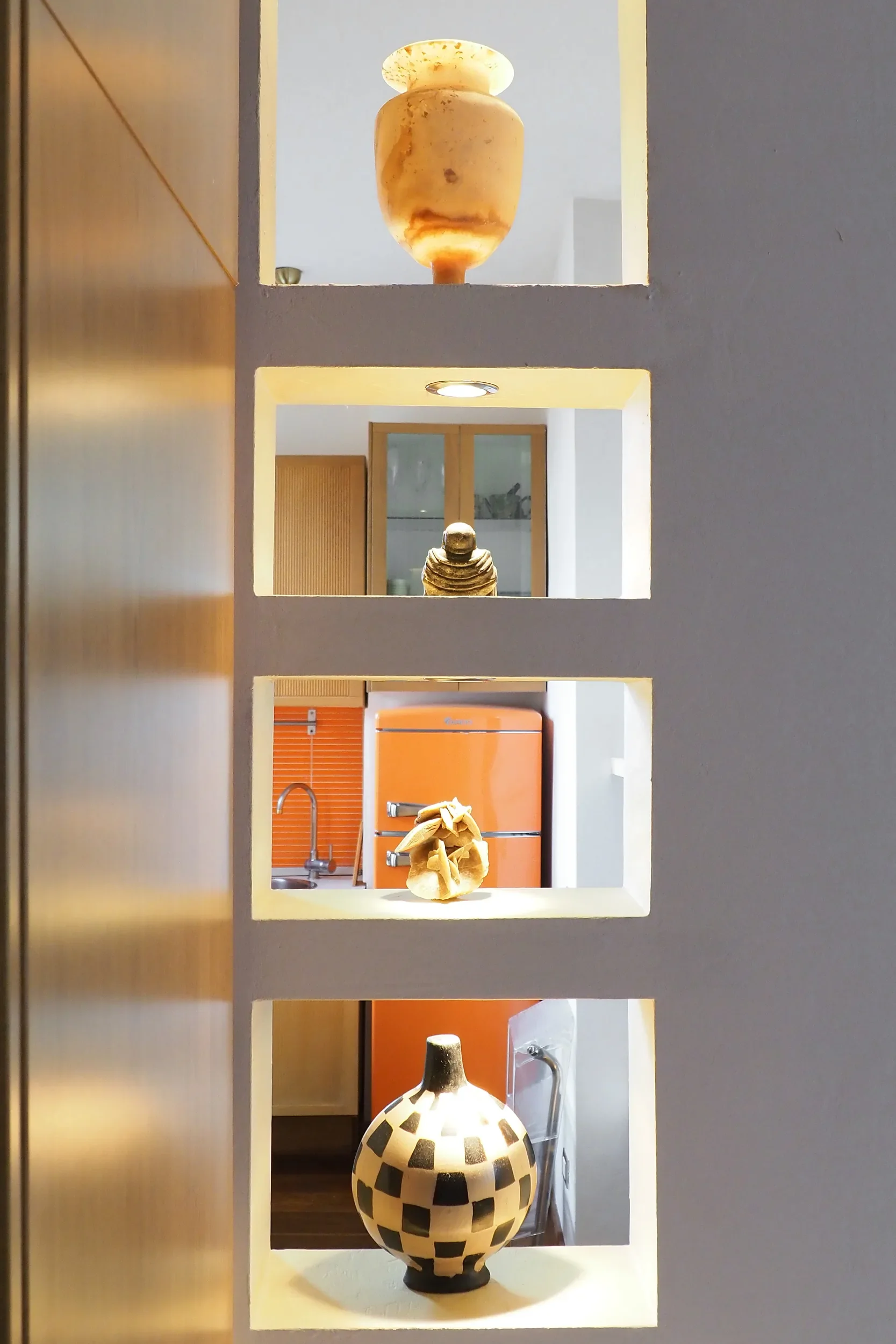 Lit niches with collected objects, ceramics and a checkerboard vase