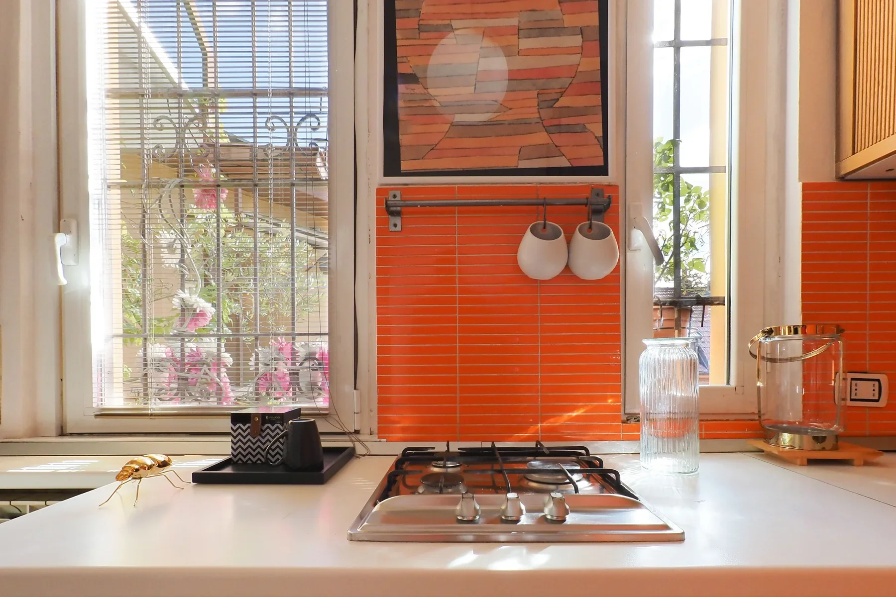 Kitchen corner with orange Porcellanosa tiles, a Rothko print toned to the tiles, and the hob under the wrought-iron window, Milano