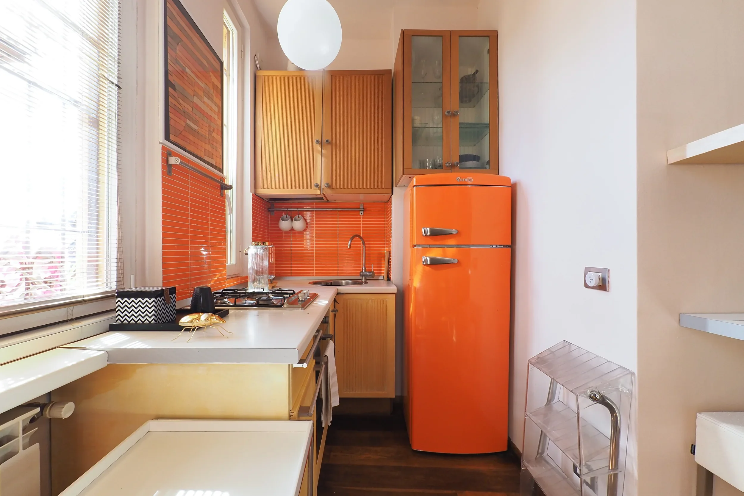 Open kitchen with an orange fridge against the orange Porcellanosa backsplash and the Rothko print above
