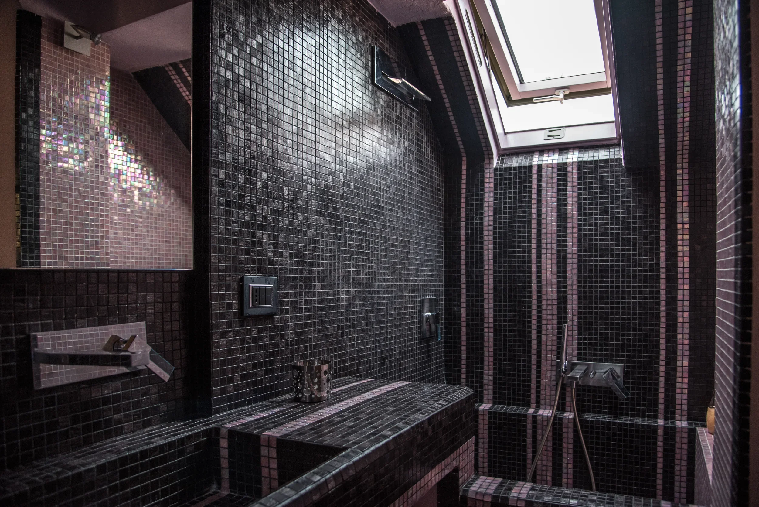 Black Bisazza mosaic bathroom under the arched skylight, with Fantini taps and the tiled bench