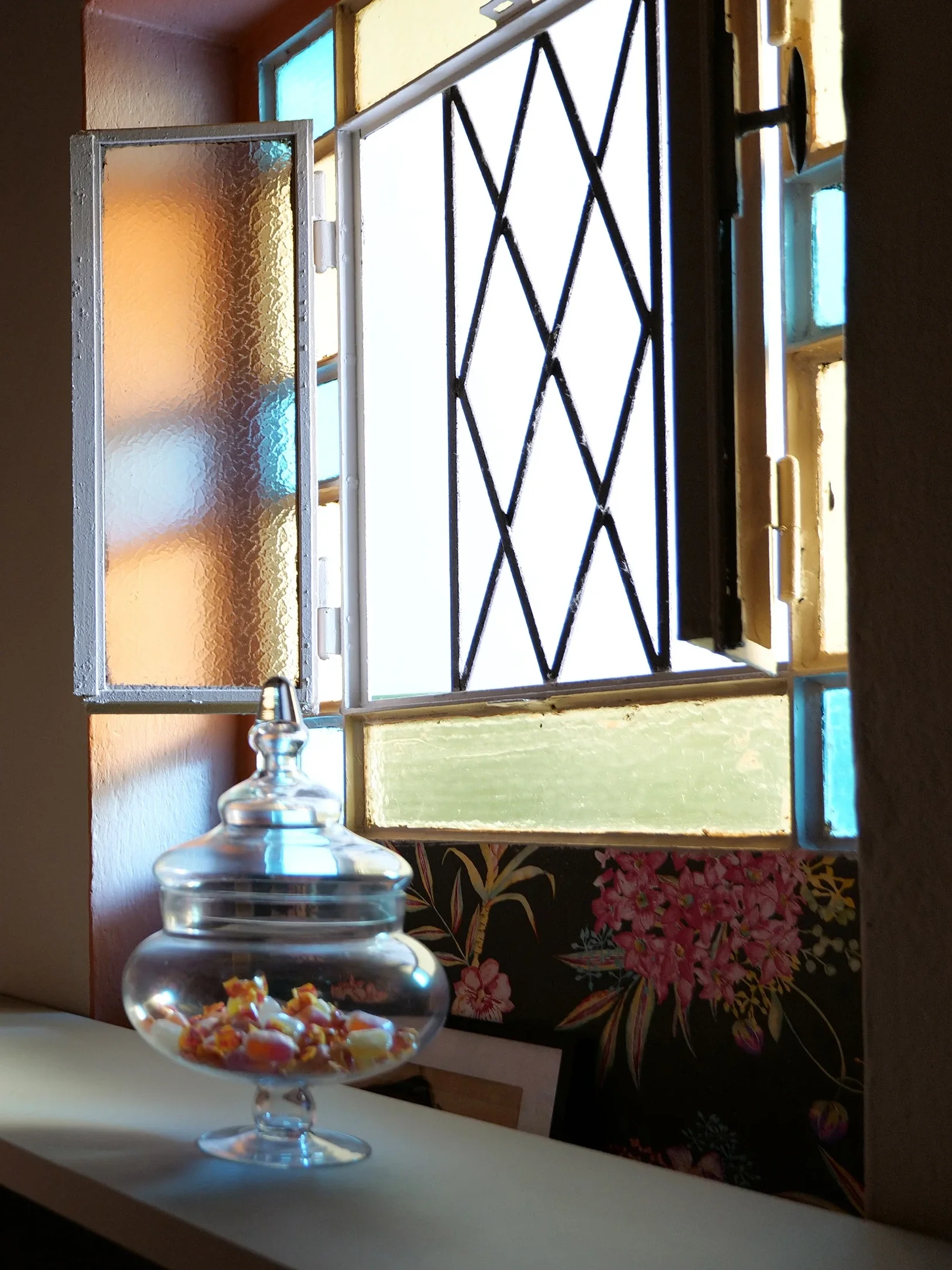 Original leaded window with coloured glass panes and a glass candy jar on the console