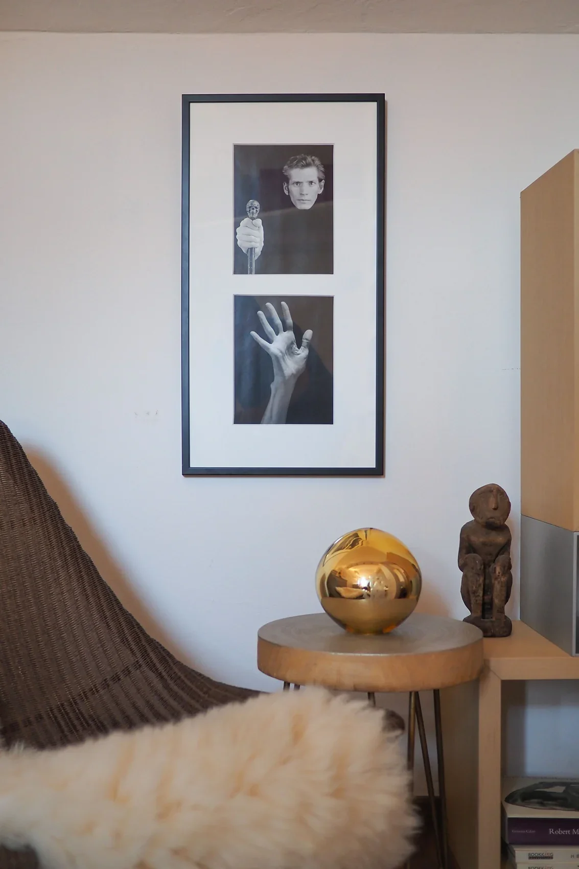 Framed Robert Mapplethorpe photographs above a gold sphere and a carved wooden figure