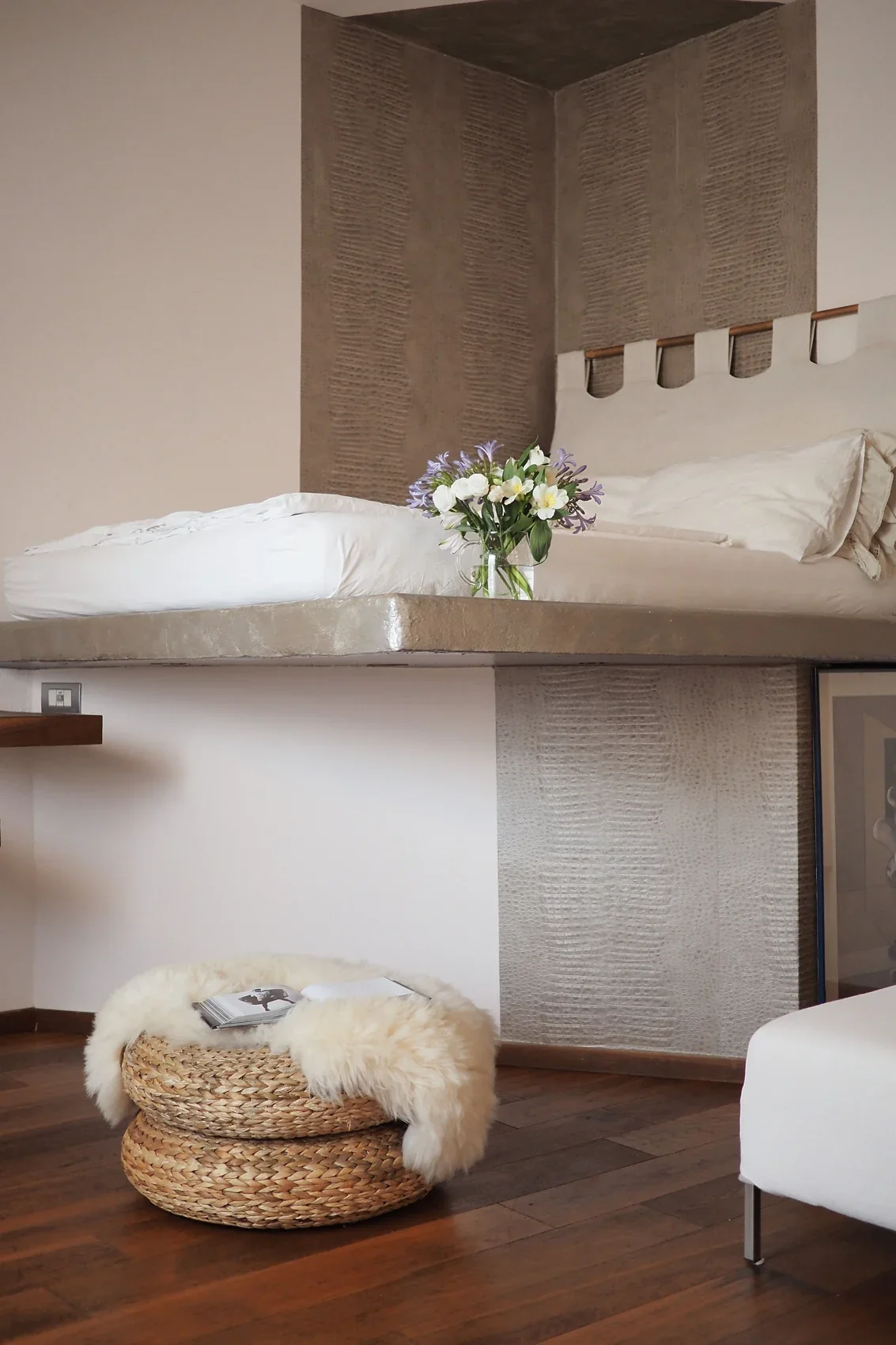 Mezzanine bed on a concrete slab with wall-mounted wooden treads, a wicker pouf and sheepskin below, Studio Sarpi Loft, Milano