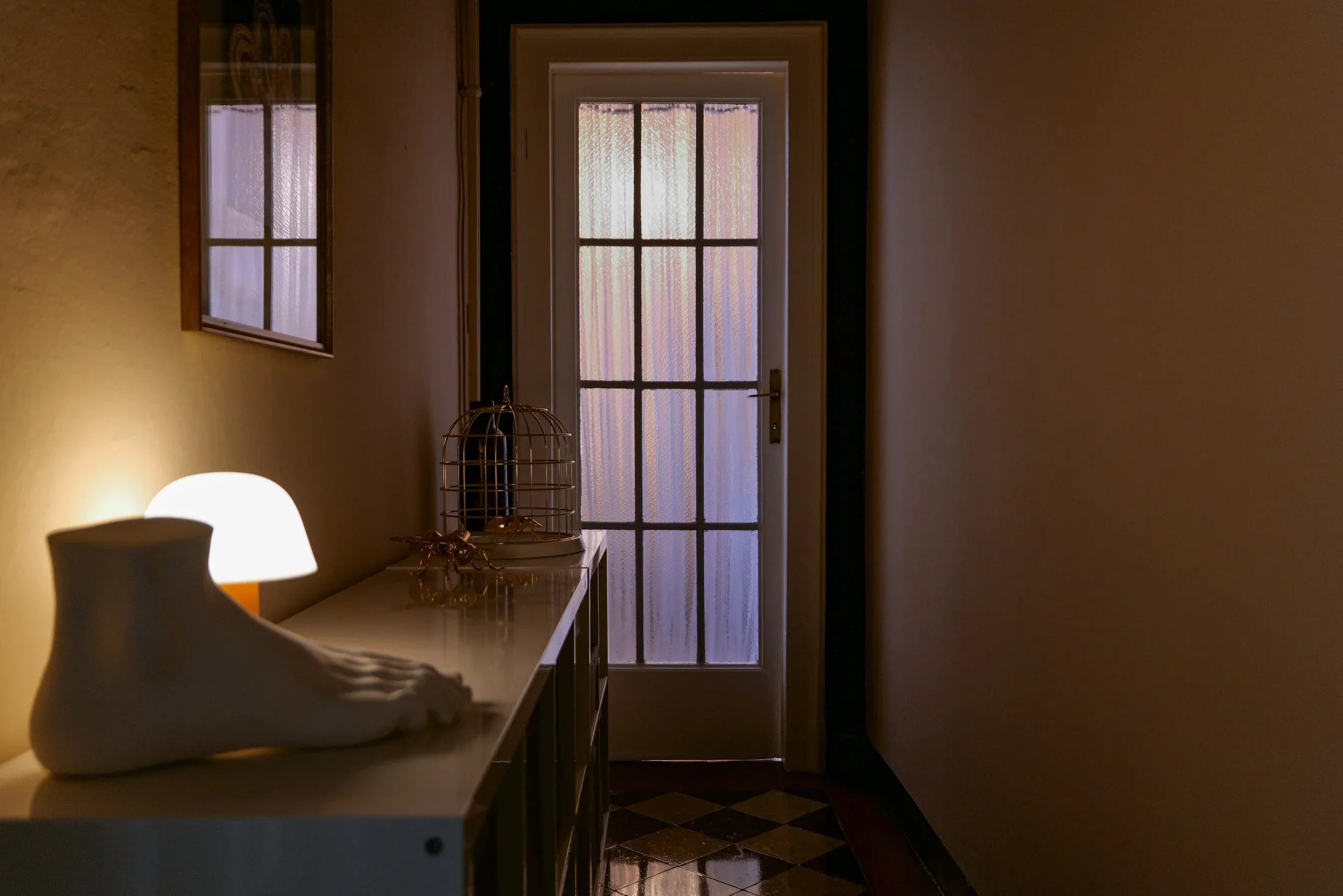 Glazed door of the bathroom with Seletti foot sculpture, Jaime Hayon Setago lamp for &Tradition and brass birdcage on the console, House of Frames bed & breakfast, Milan